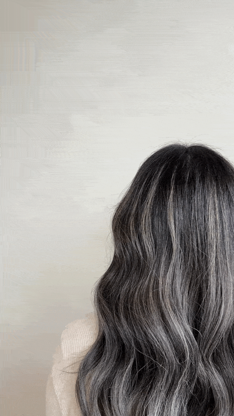 A woman with long, wavy, black and gray ombre hair standing in front of a white wall.