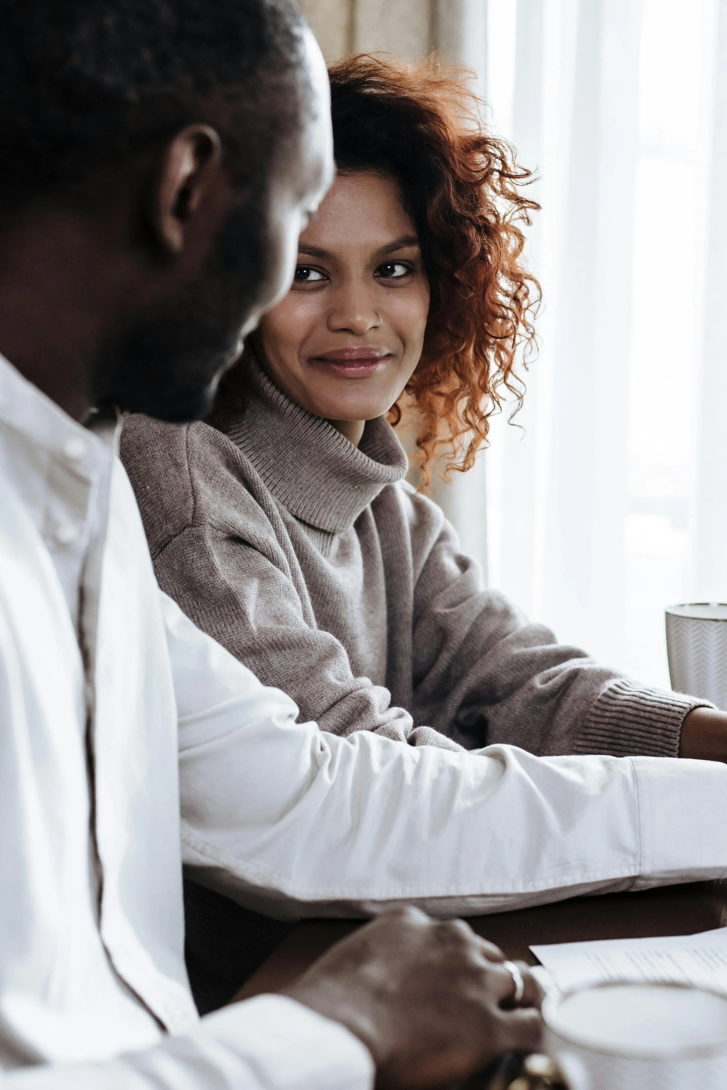 Two people sitting together, one looking toward the other with a soft, attentive expression.