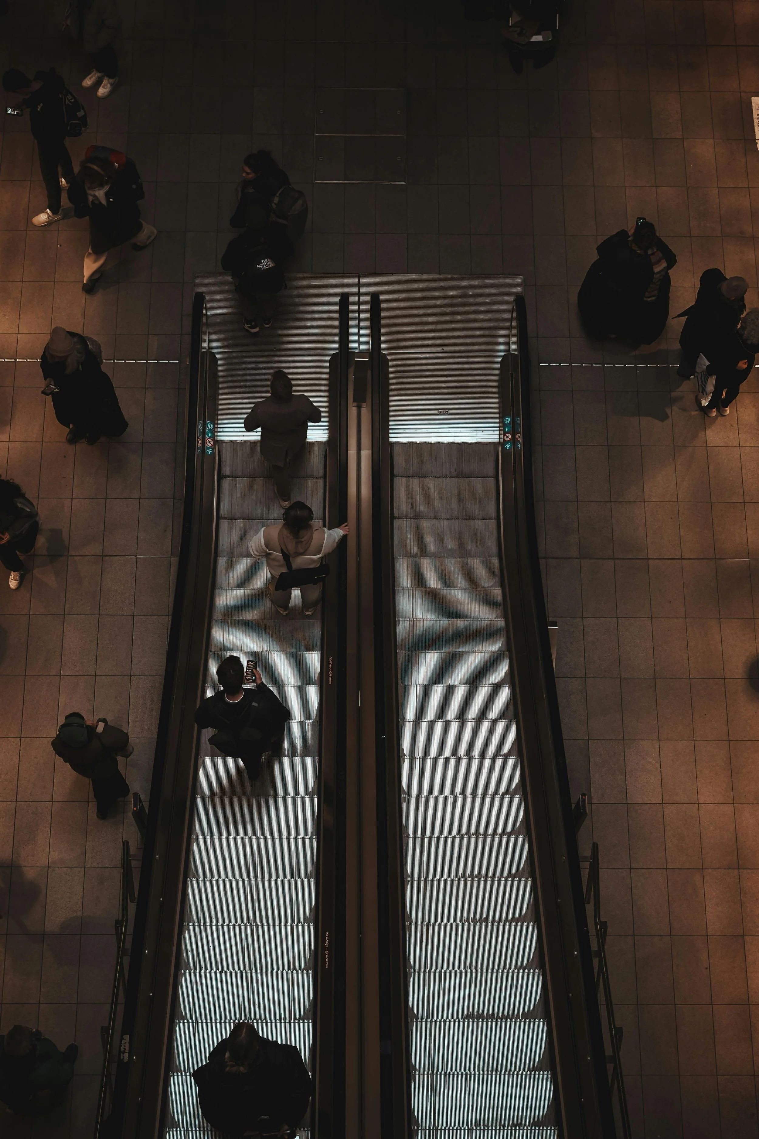 People on two parallel escalators in a busy transit station, moving in opposite directions