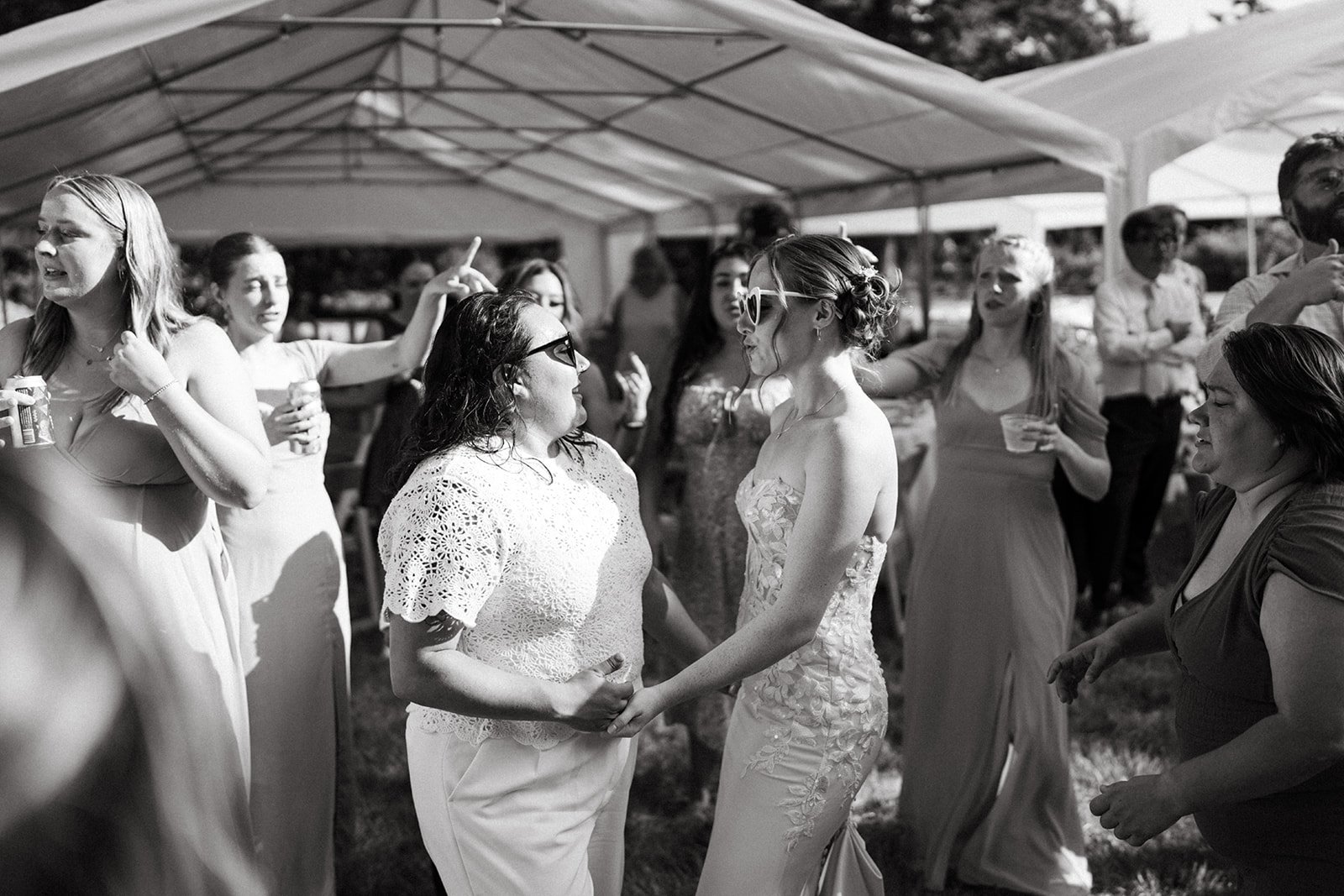 Black and white photo of women dancing and socializing at an outdoor event under a large tent.