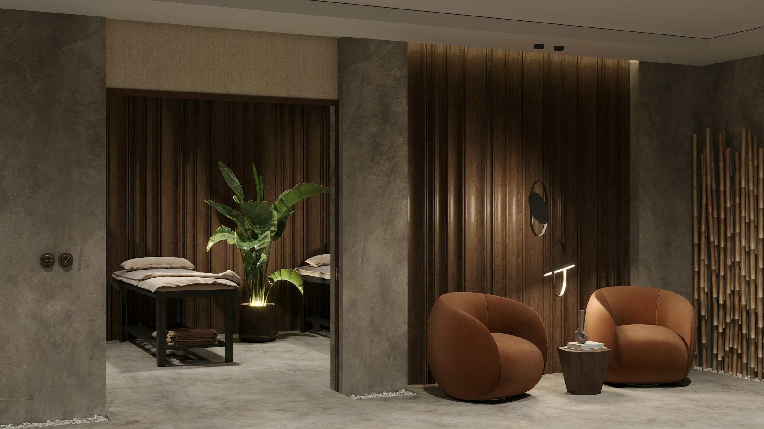 A modern interior space with warm lighting, featuring a sitting area with two brown armchairs, a small side table with a decorative vase, and a wooden wall accent. There is a partition with a door leading to a bedroom area with a bed, pillows, and a large green potted plant.