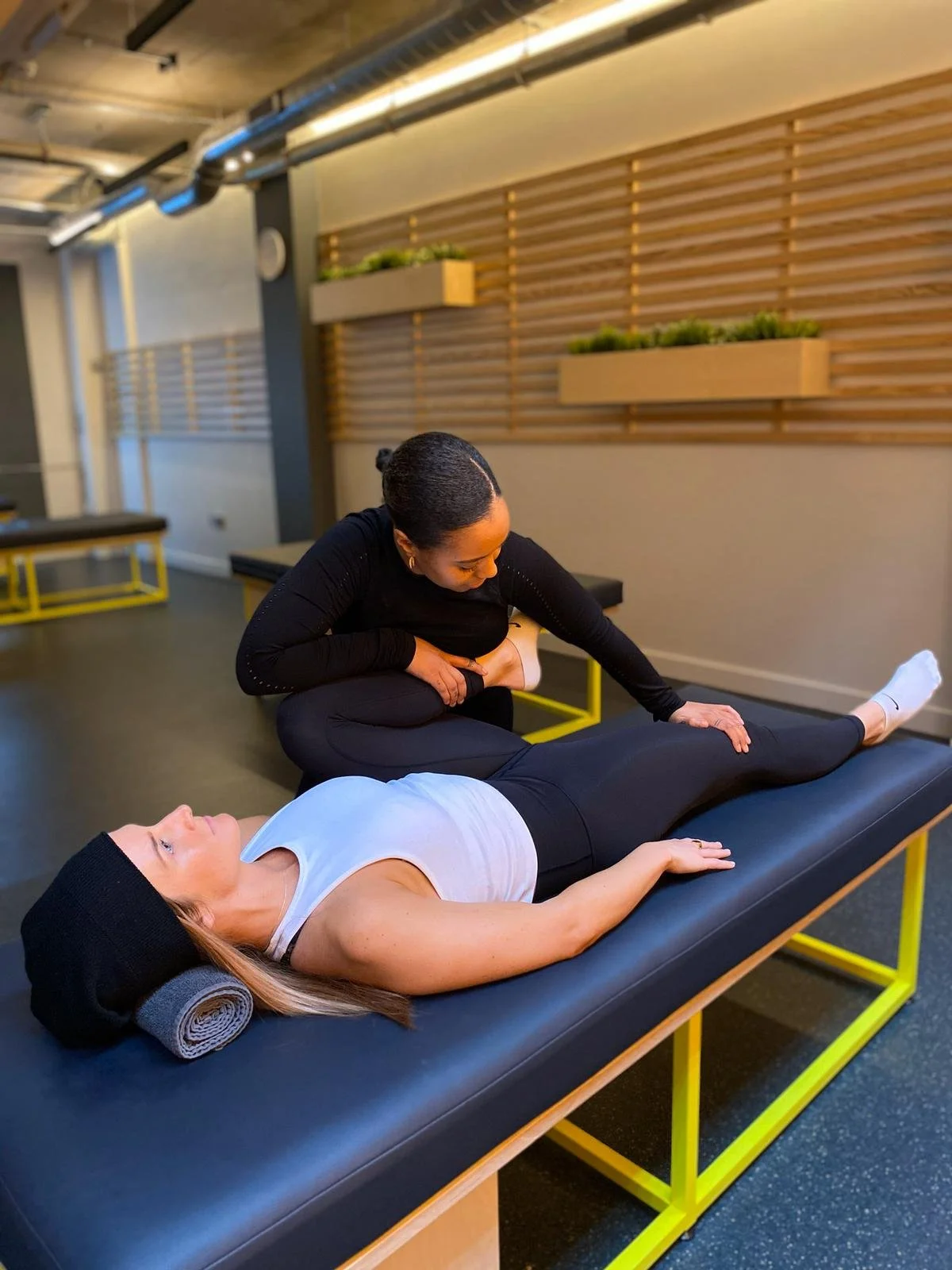 A person receiving physical therapy for her leg, lying on a treatment table with a therapist stretching her leg in a wellness or therapy center.