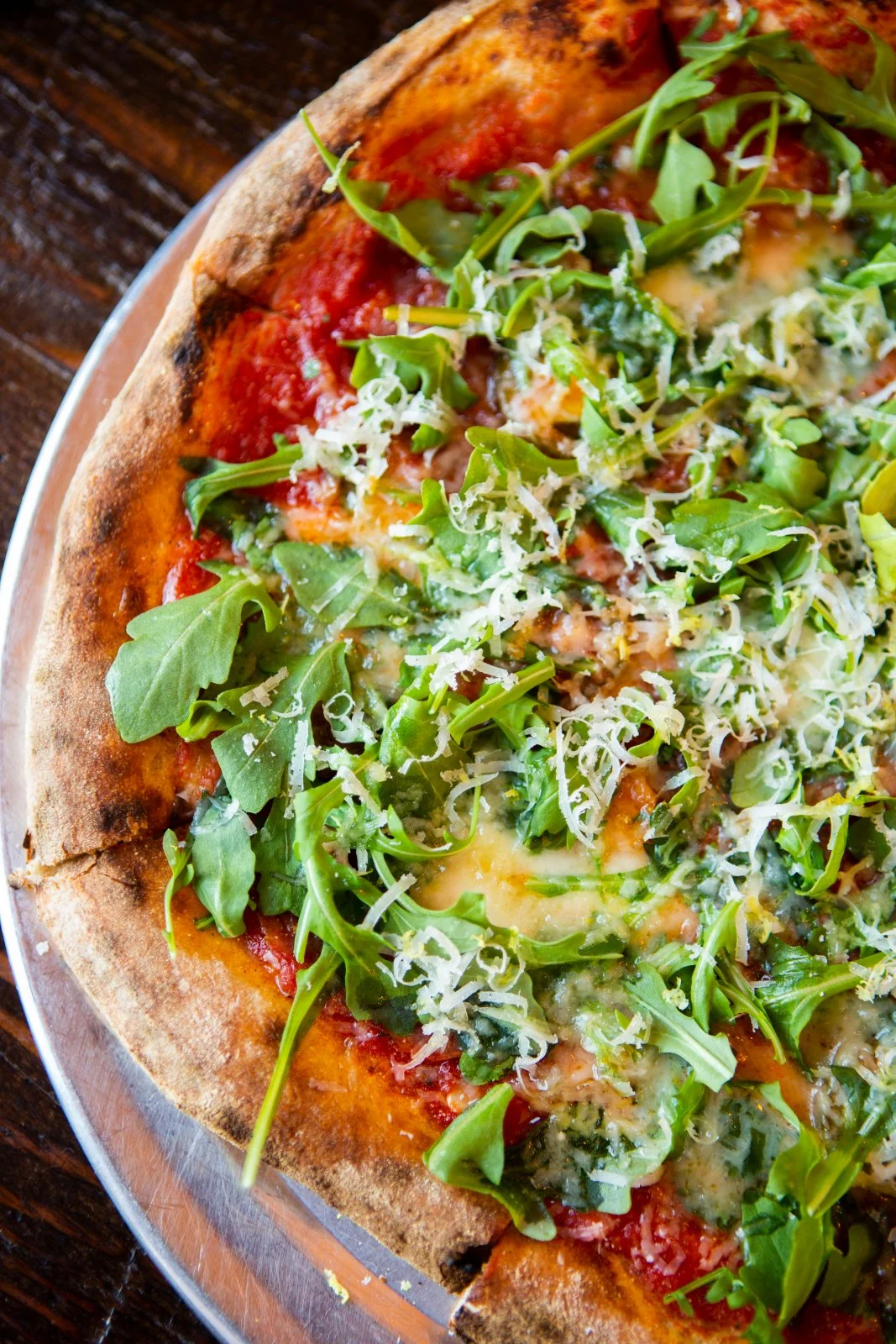 A person uses a pizza cutter to slice a freshly baked cheese pizza on a wooden table.