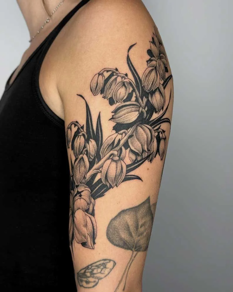 Surreal tattoo by Kuya (@kuya.tattoos) featuring a large cluster of detailed blooming flowers on the upper arm, with additional tattoos of a leaf and a butterfly on the lower arm.