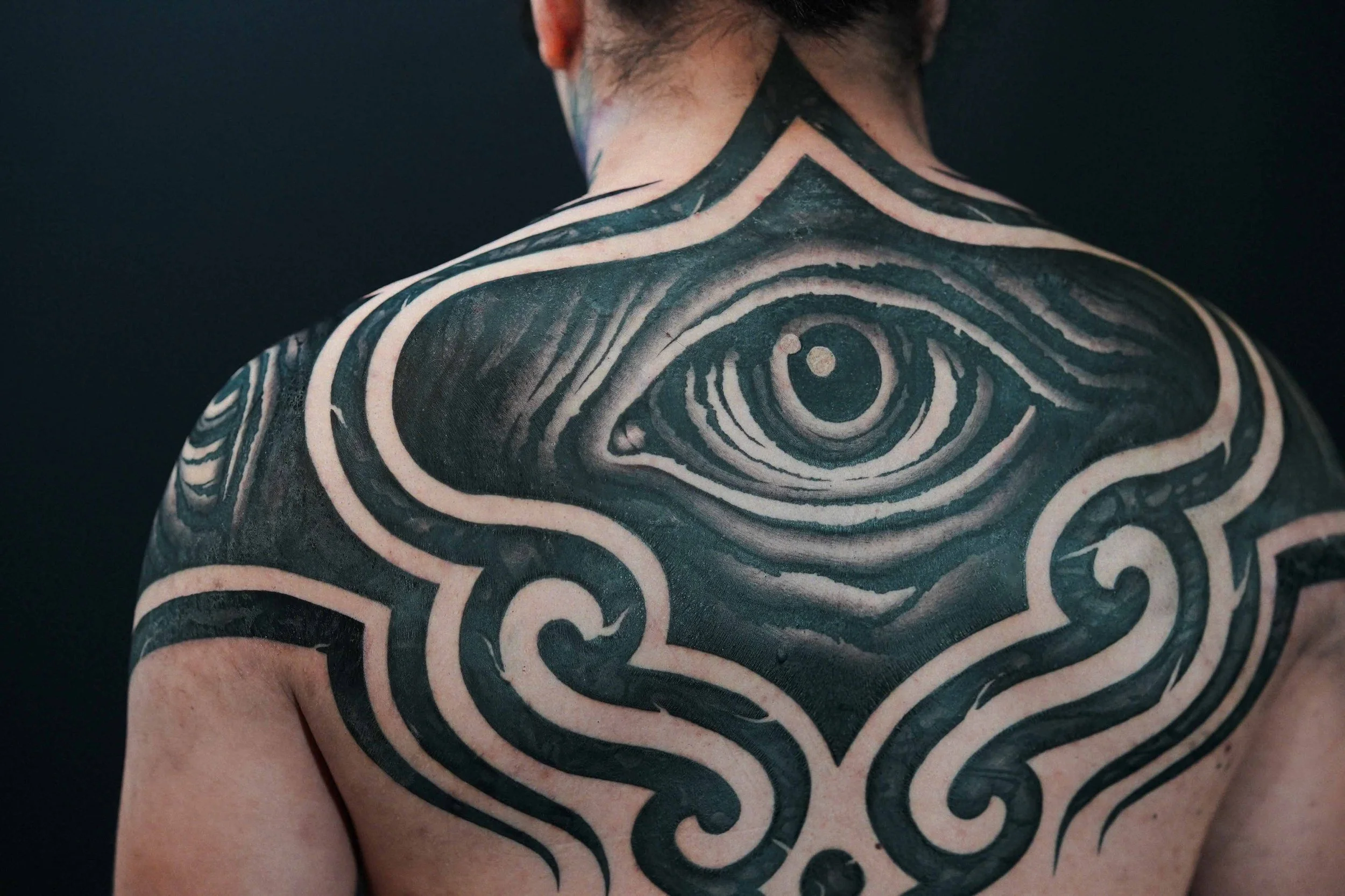 Giant eye ornamental tattoo featuring symmetrical eyes on the shoulder caps.
