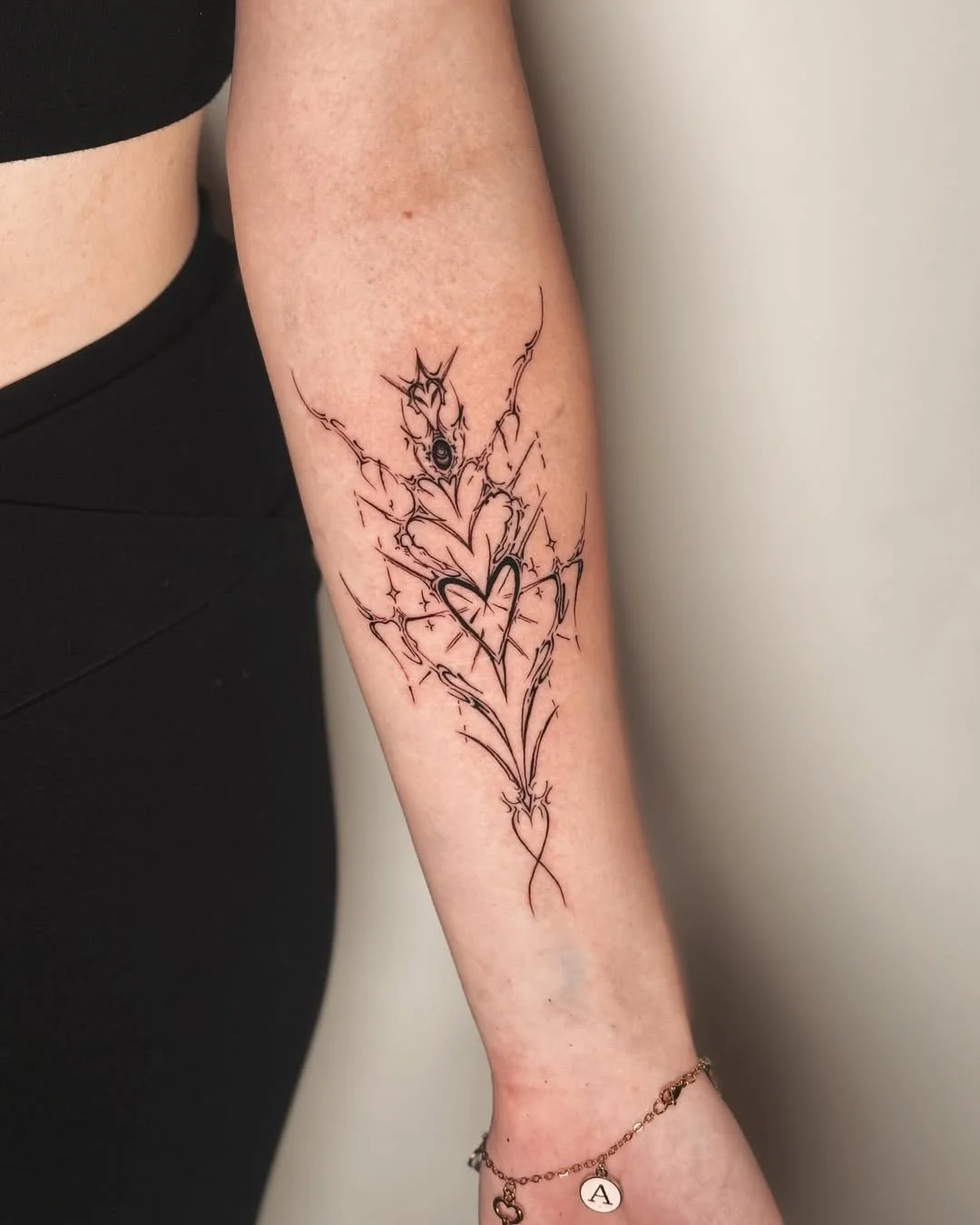 Blackwork cybersigilism heart wrapped in thorns and sparkles — a y2k-meets-gothic forearm piece. By Stella Sanchez (@umbra.inks), now booking at Dark Water Tattoo Studio in Berkeley, CA.