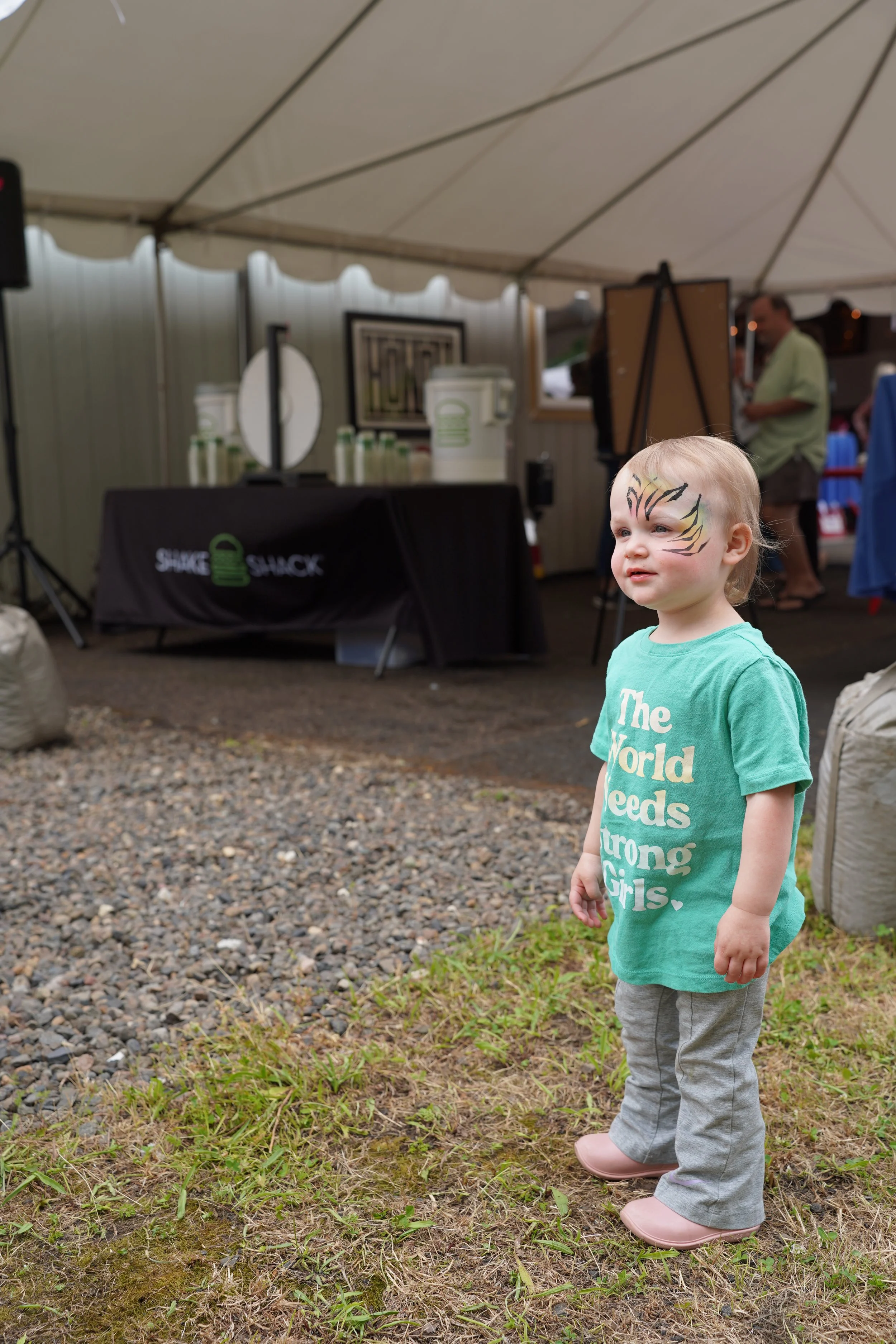 Toddler with painted tiger face standing outside smiling.
