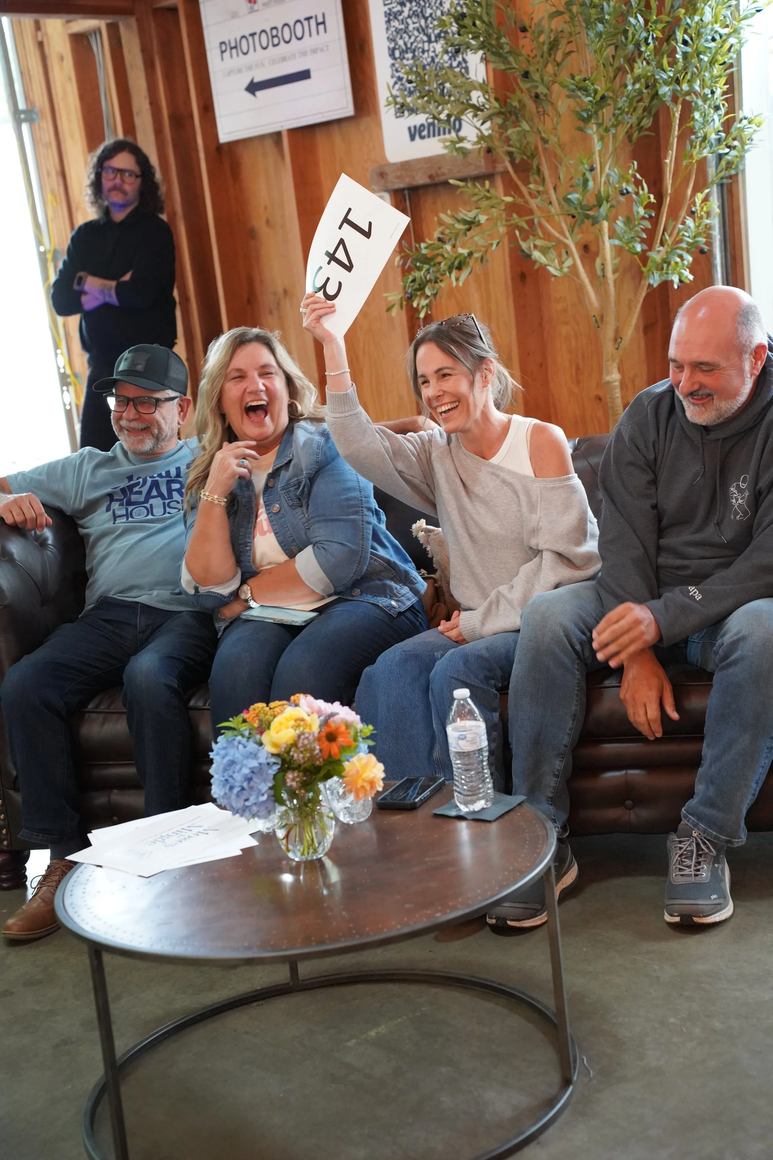 Two men and women sitting on a couch bidding and smiling at Mosey & Mingle Auction.
