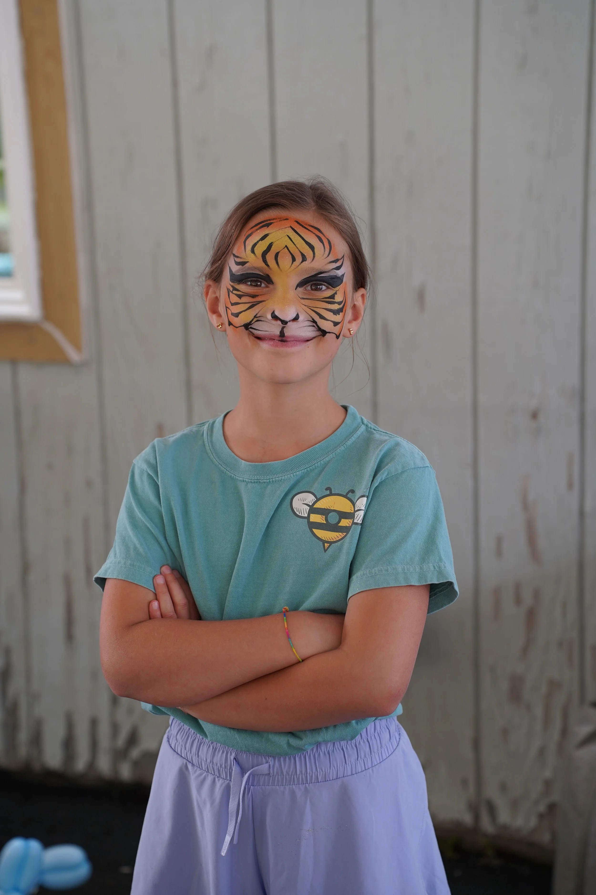 Young girl in full tiger face paint smiling at camera.