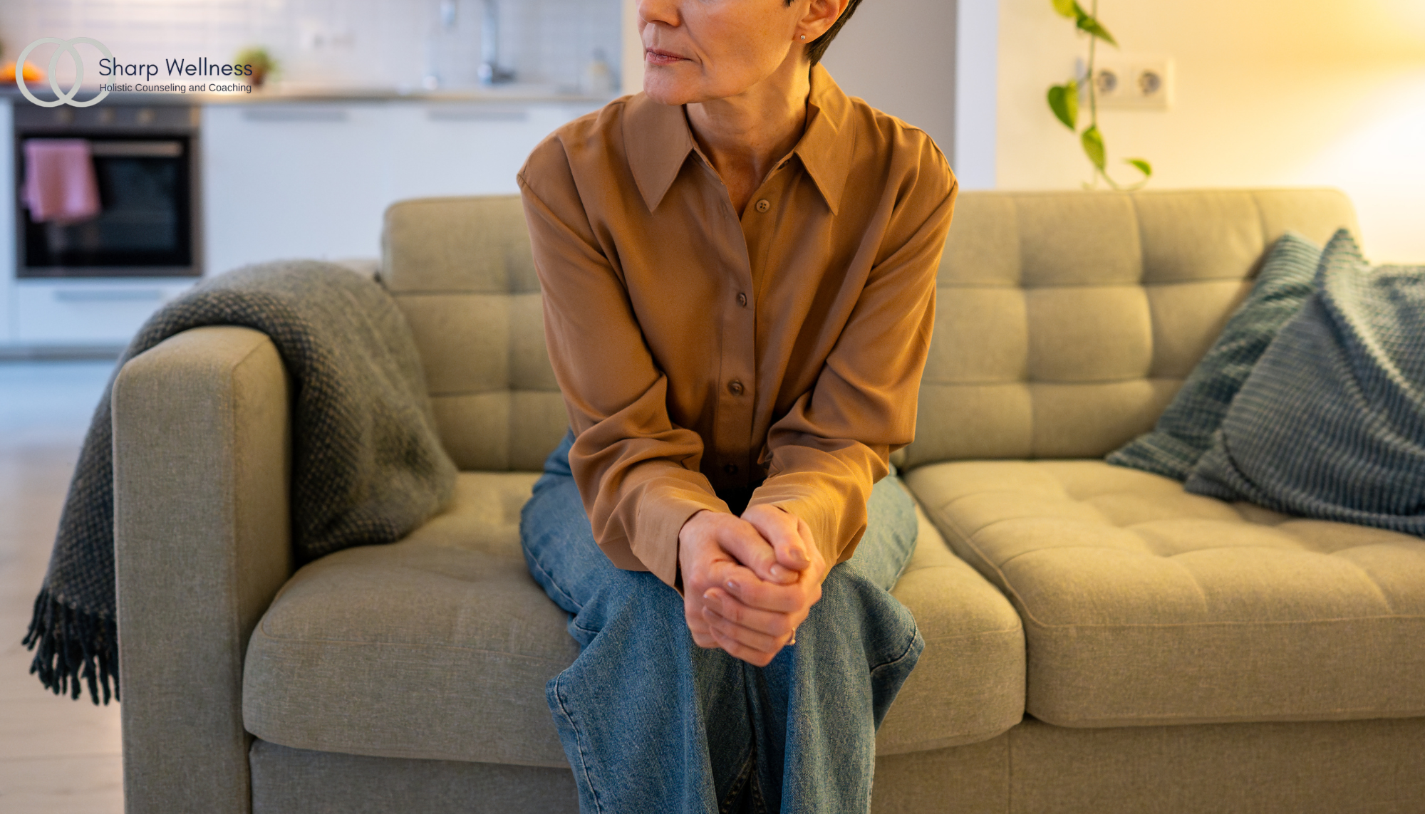 Woman sitting alone on a couch with clasped hands, representing anxiety, stress, overthinking, and emotional overwhelm.