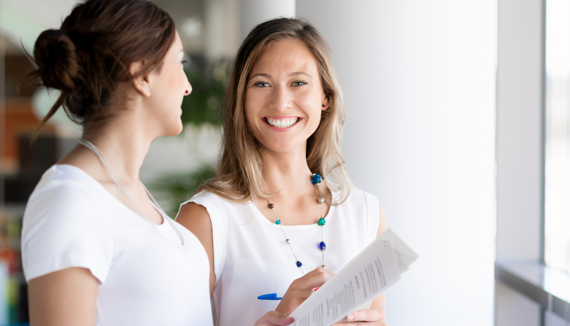 Two women talking in a professional setting, representing workplace pressure, people pleasing, perfectionism, approval seeking, and therapy for healthier boundaries and self-confidence.