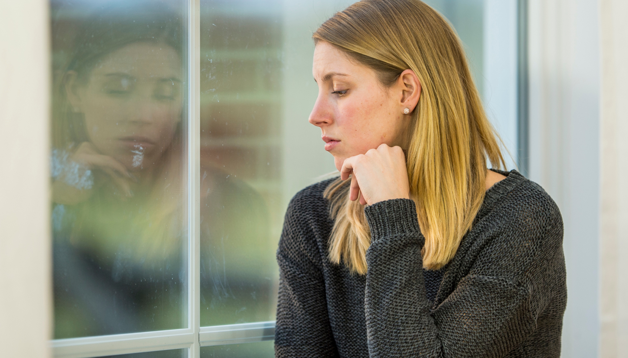 Woman sitting by a window appearing deep in thought representing trauma, emotional healing, and mental health counseling support.