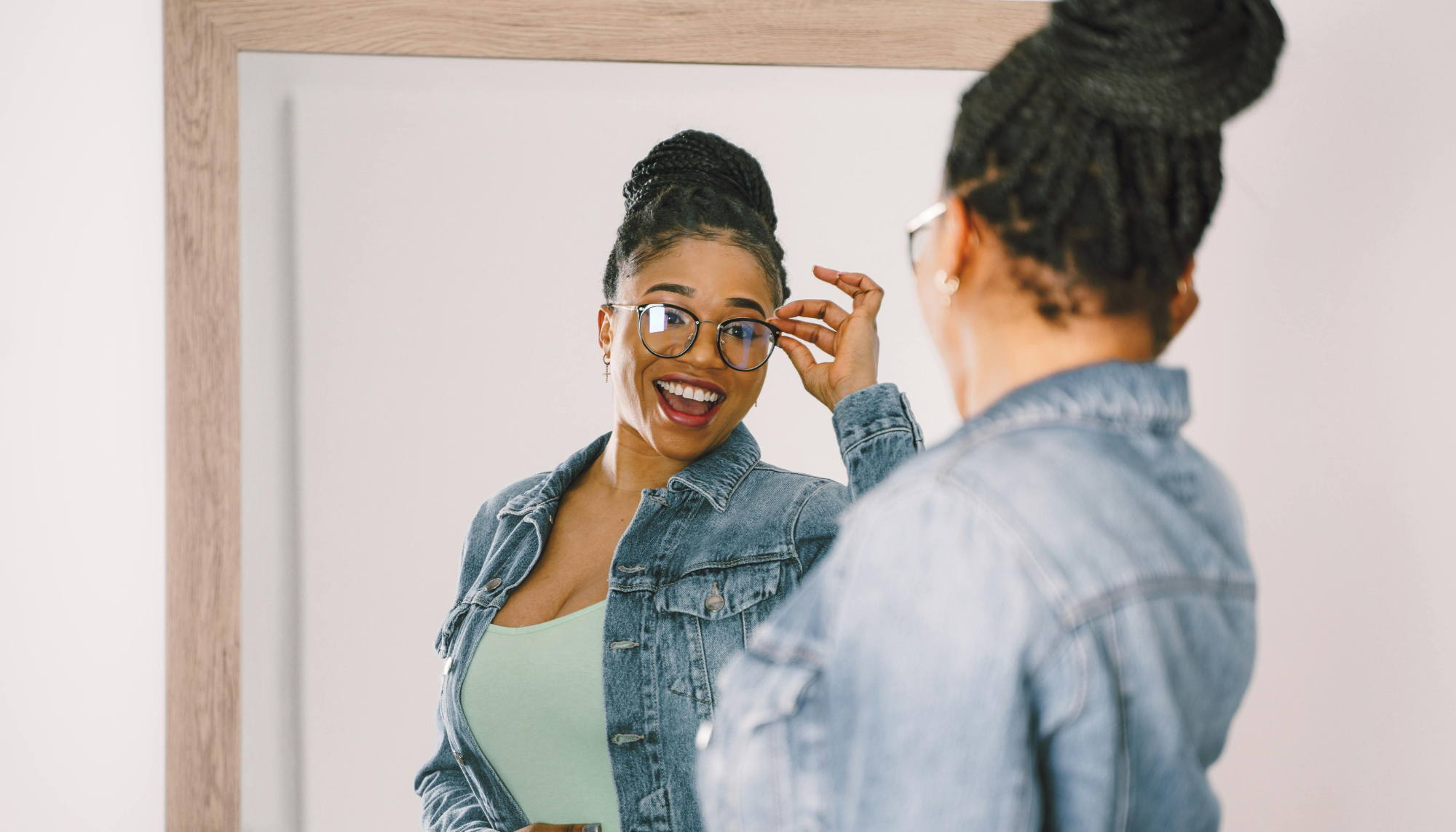 Woman smiling at herself in the mirror, representing improved self-esteem, confidence, self-worth, and personal growth through therapy.