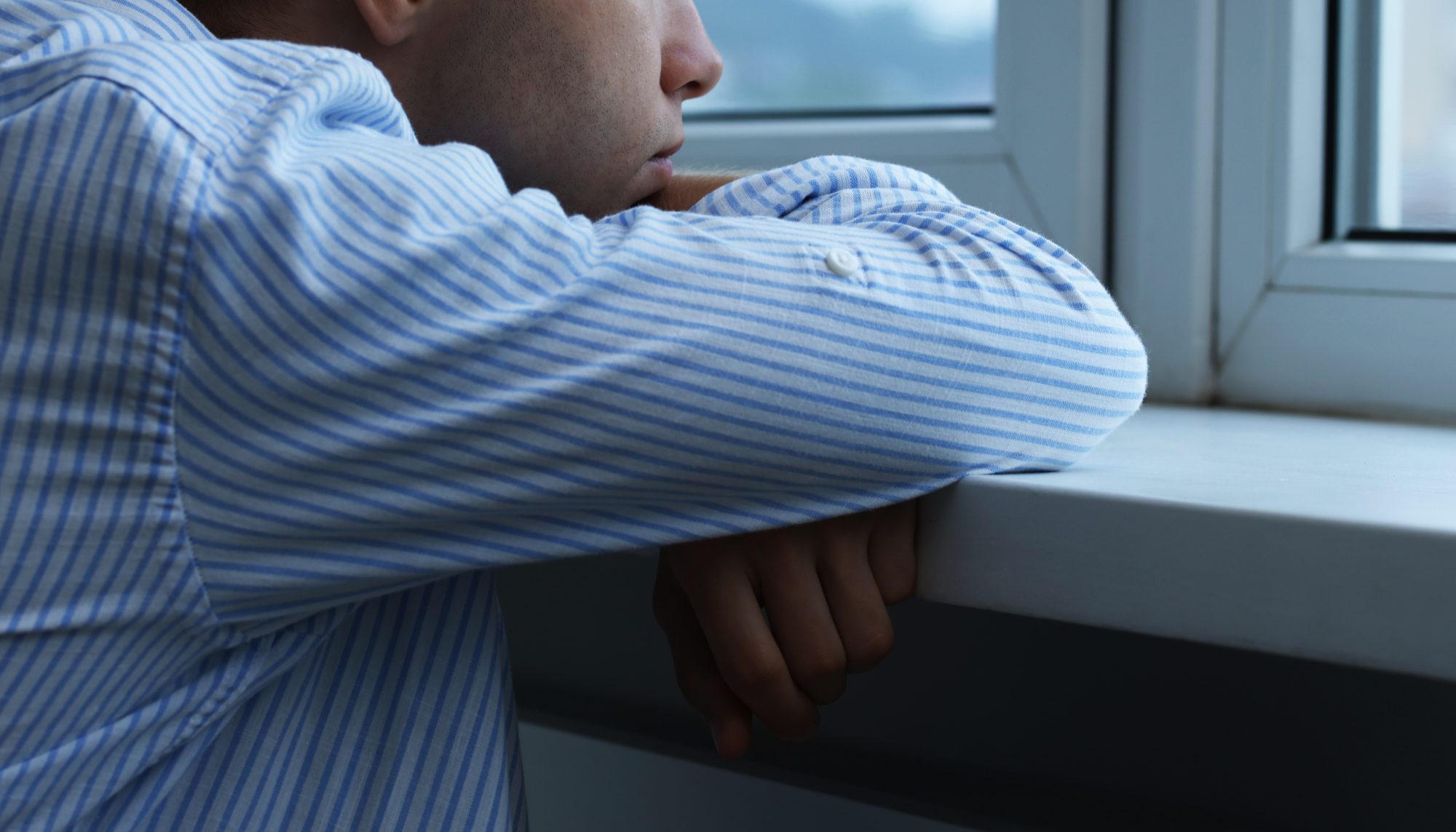 1. Man looking out a window with a somber expression, representing depression, loneliness, low motivation, and emotional struggles.