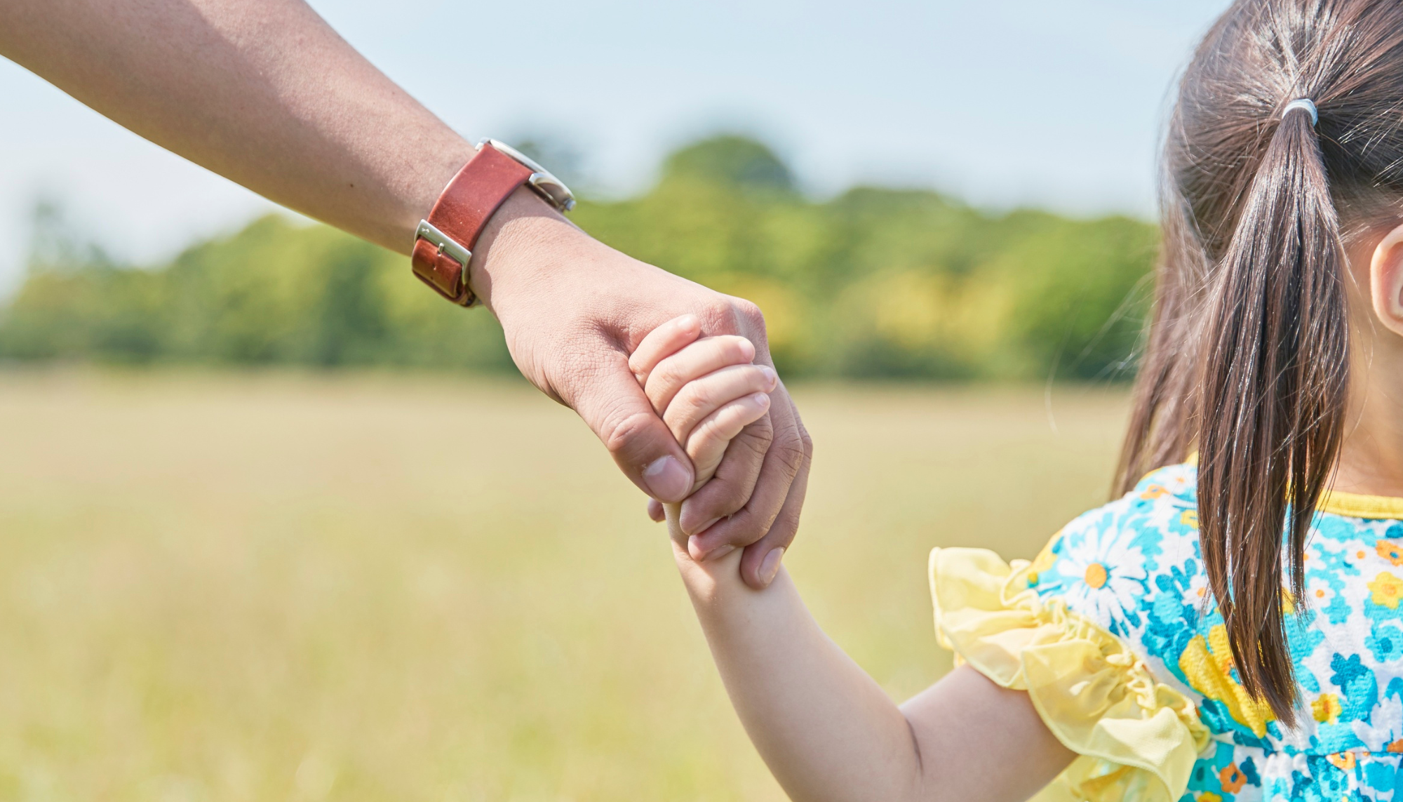 Parent holding a young child’s hand outdoors, representing parenting support, healthy attachment, and parent therapy for families.
