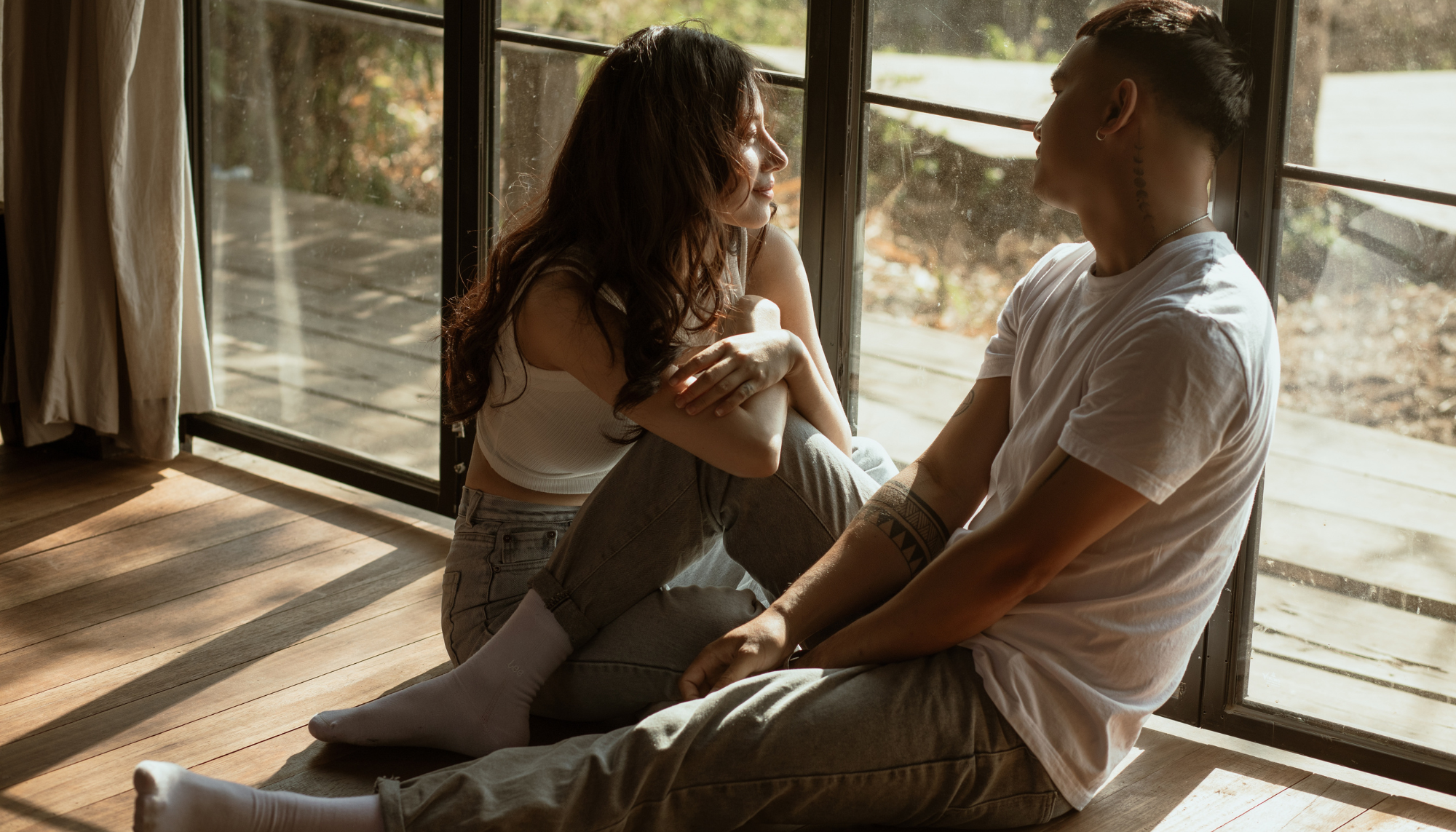 A couple sitting together by a sunlit window, sharing a quiet moment of connection—reflecting the openness and communication at the heart of couples therapy.