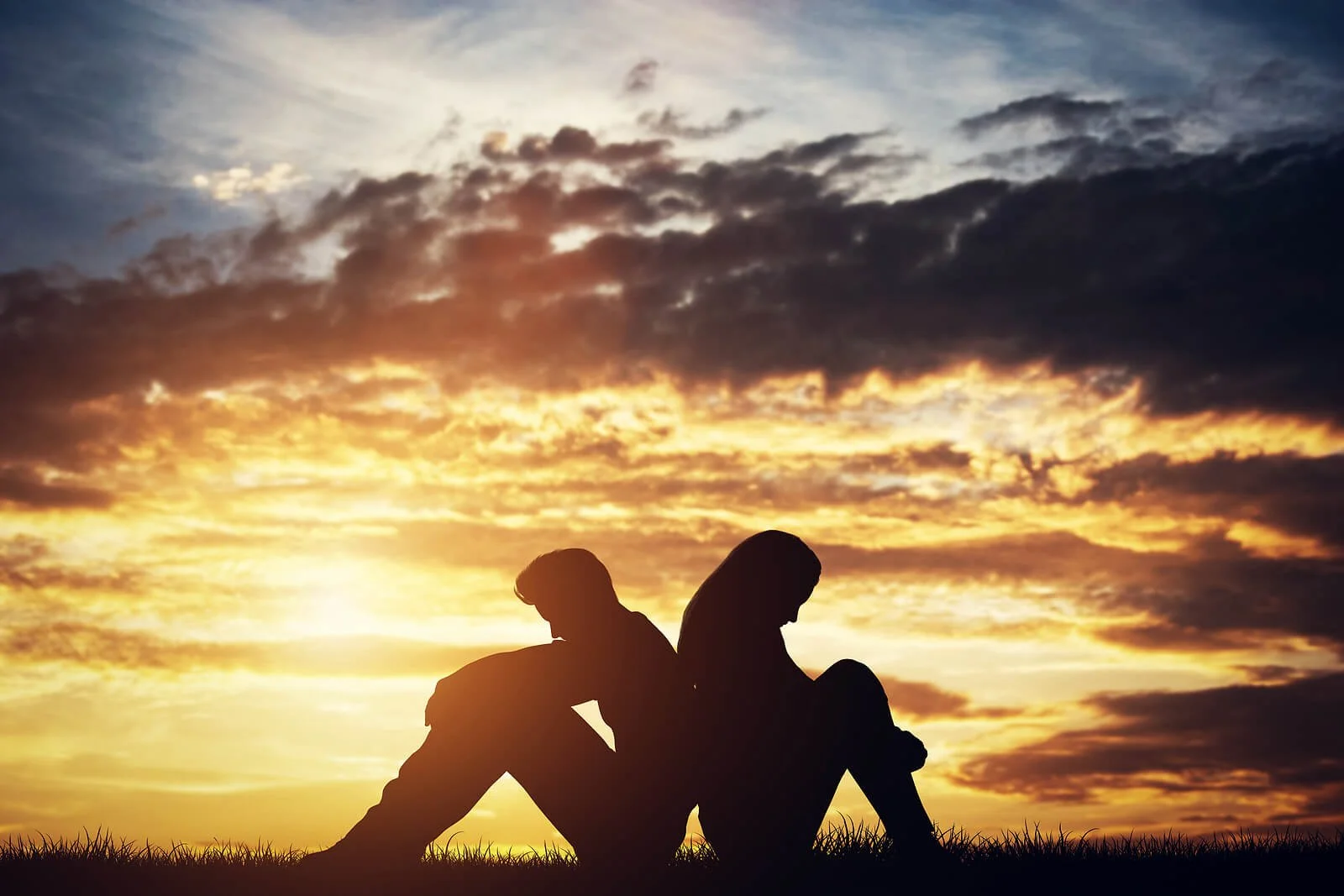 Silhouette of a couple sitting apart at sunset representing relationship struggles, healing, and couples intensive counseling services at Sharp Wellness.