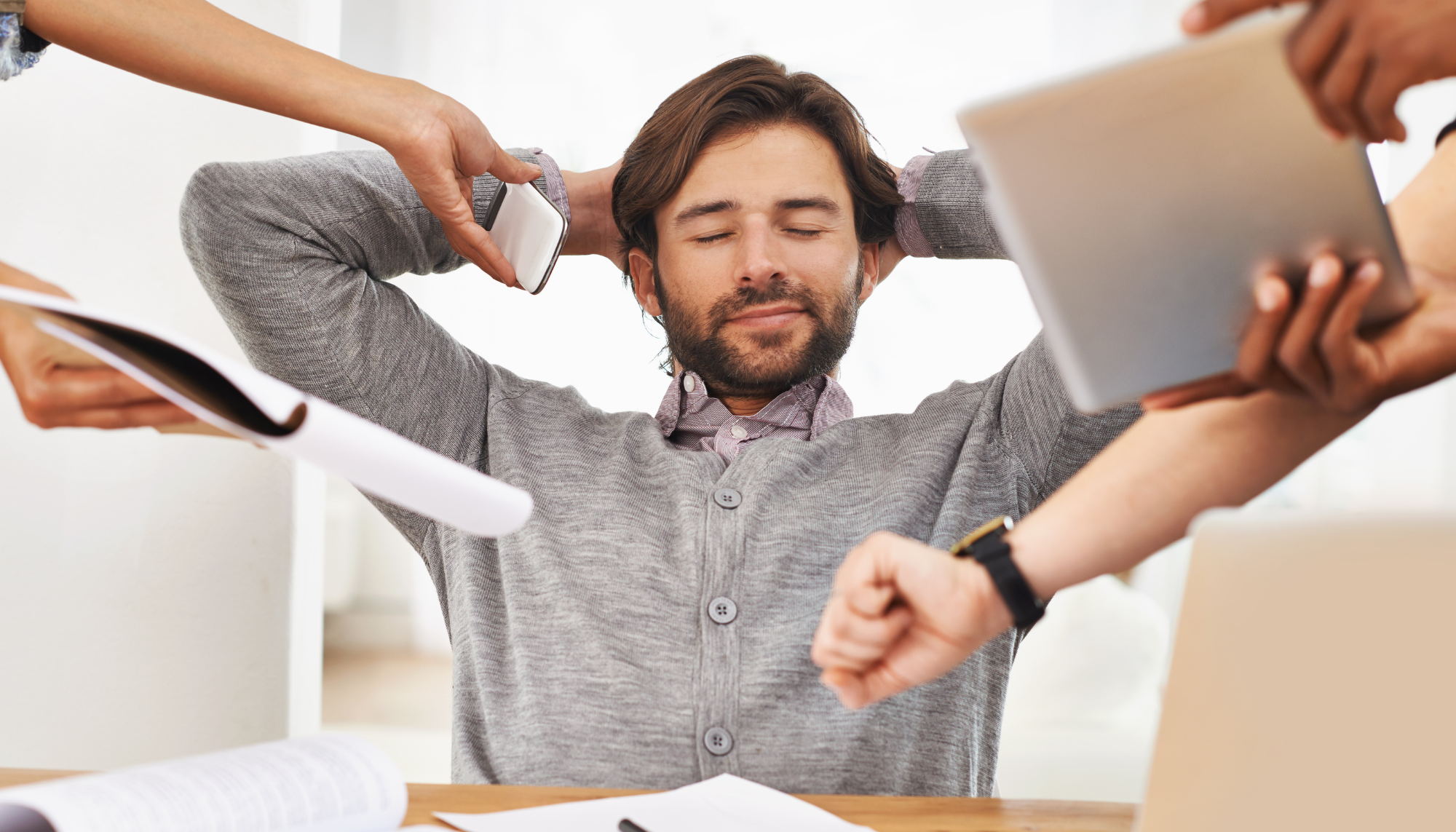 Man feeling overwhelmed at work while surrounded by phones, paperwork, and screens, representing stress, avoidance, burnout, and therapy support in Birmingham, AL.