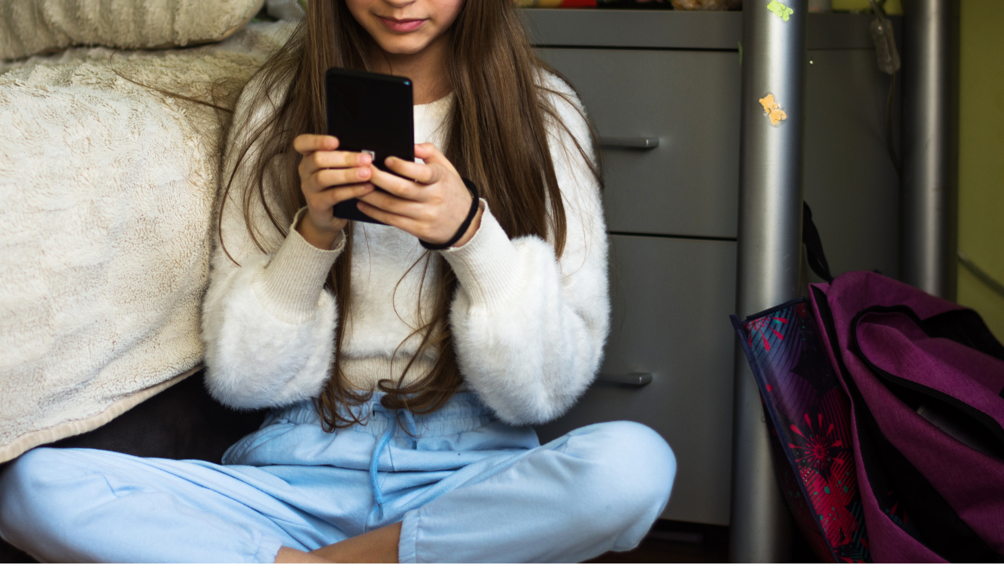 teen girl sitting on bedroom floor using smartphone alone, representing doomscrolling and social media impact on teen mental health