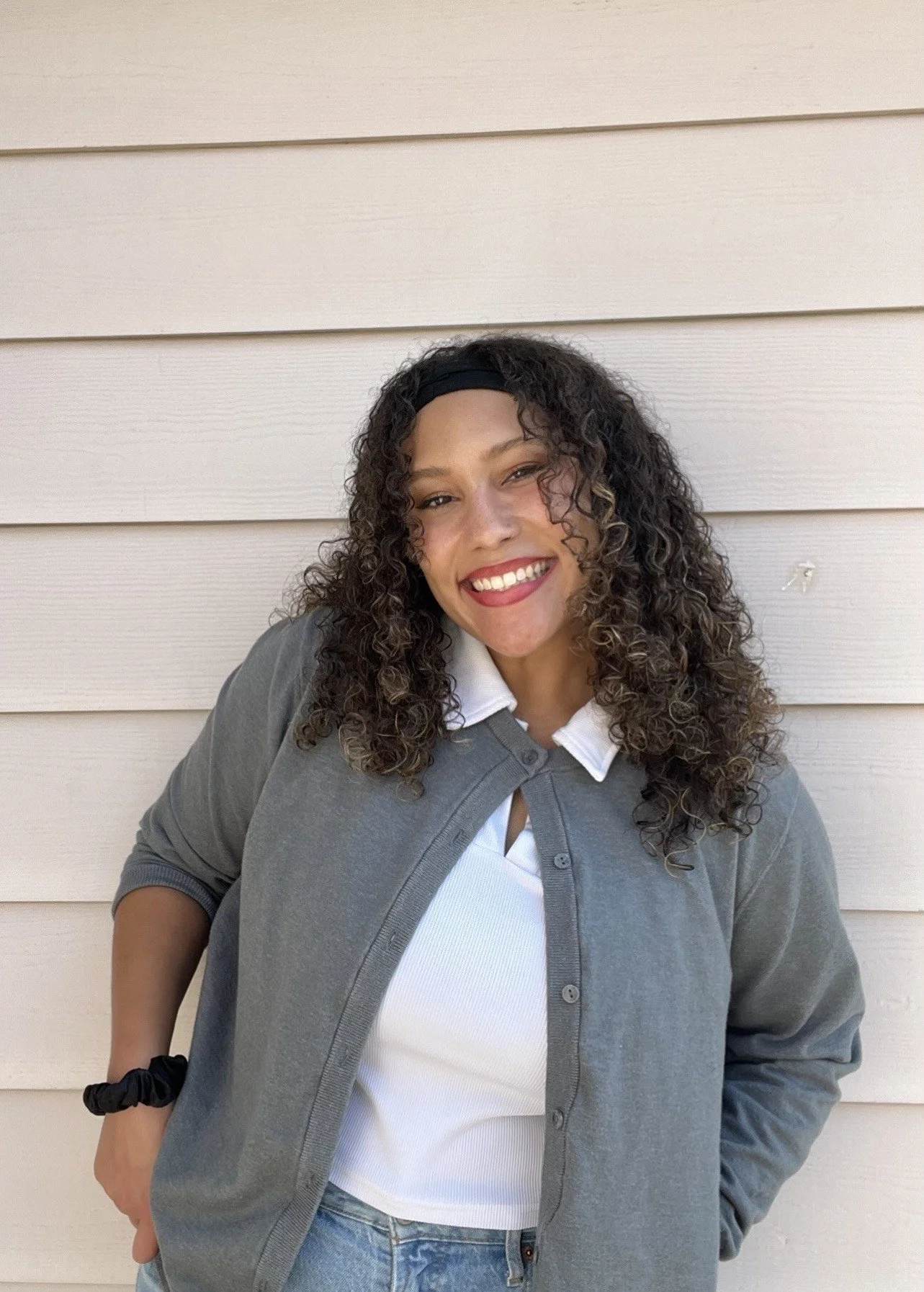 A young woman smiling against a blank background wearing a cardigan and collared shirt.