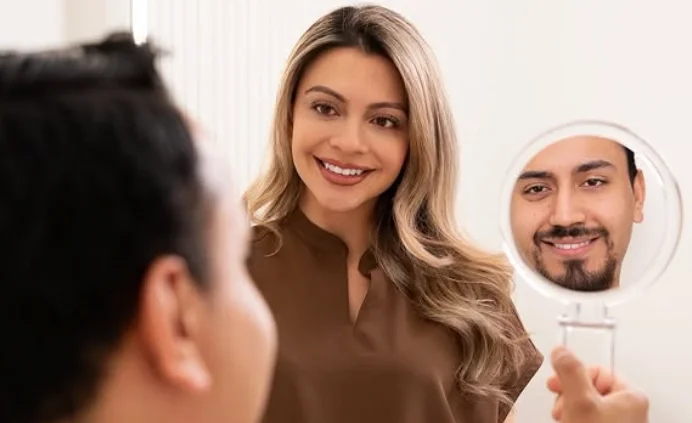 A woman looking at herself in a mirror held by a man who is partially visible in the foreground.