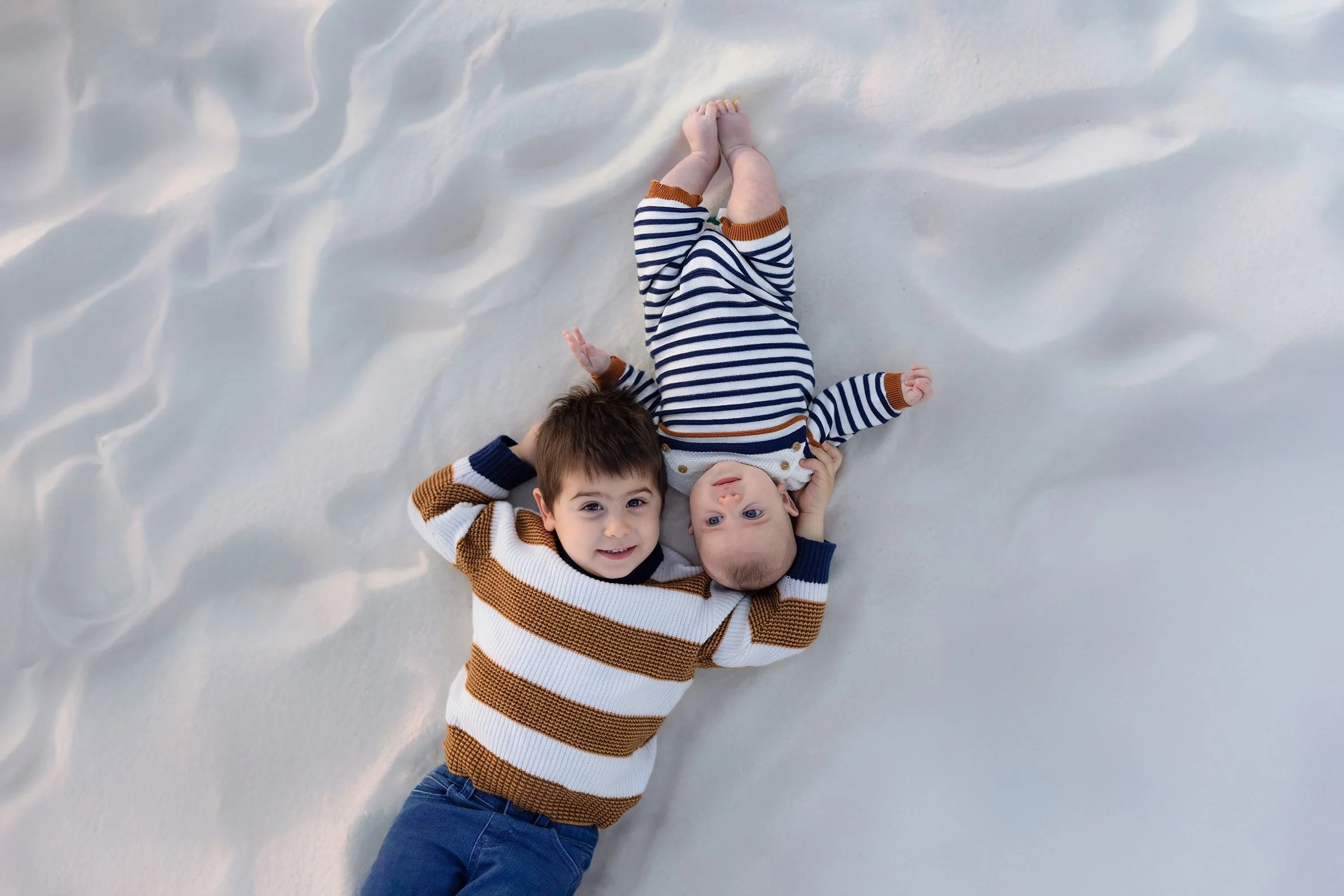 Two young boys lying in the sand at Avila Beach on the Central Coast, looking up and smiling during golden hour family photo session