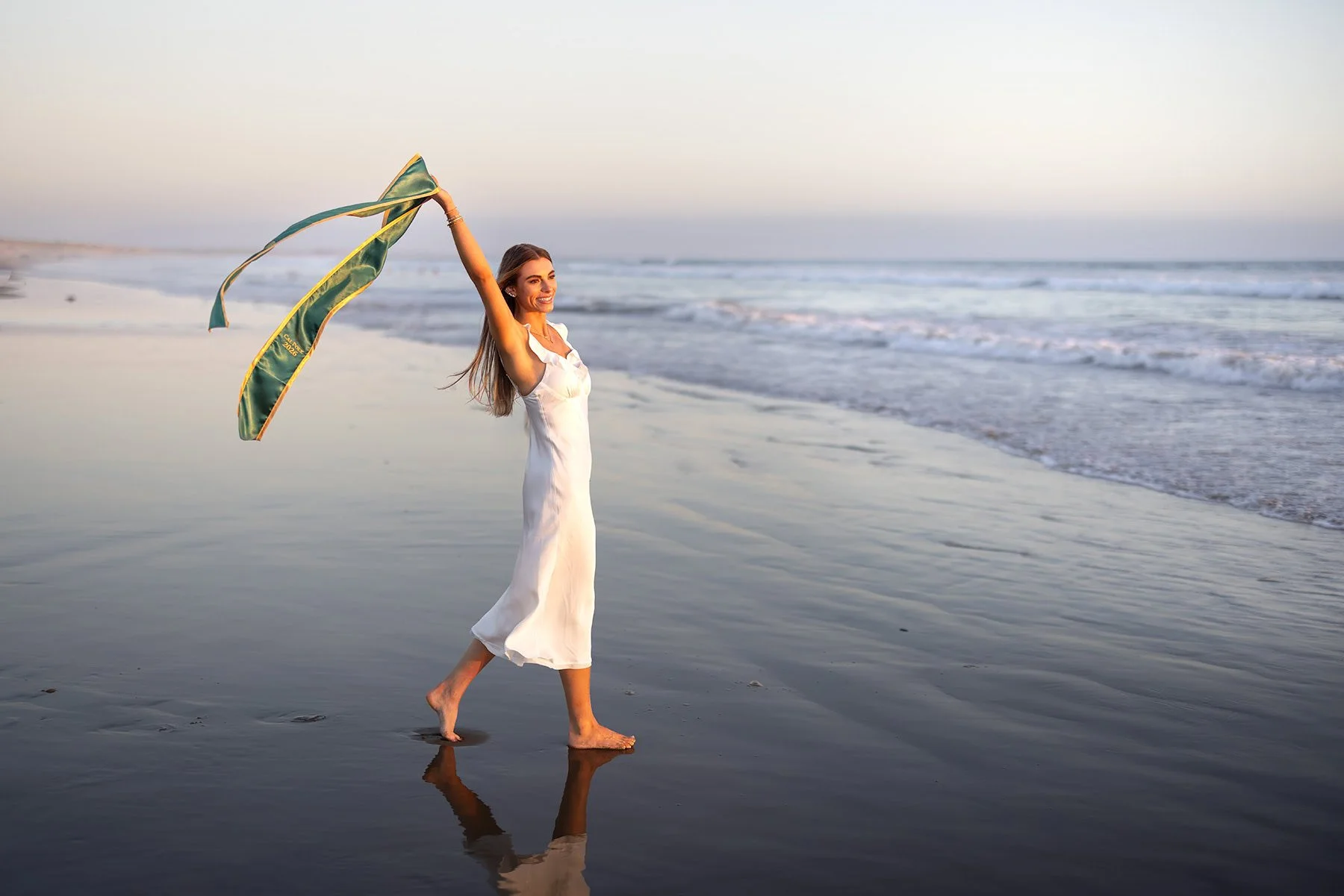Cal Poly graduate walking along the beach in a white dress during blue hour near Pismo Beach