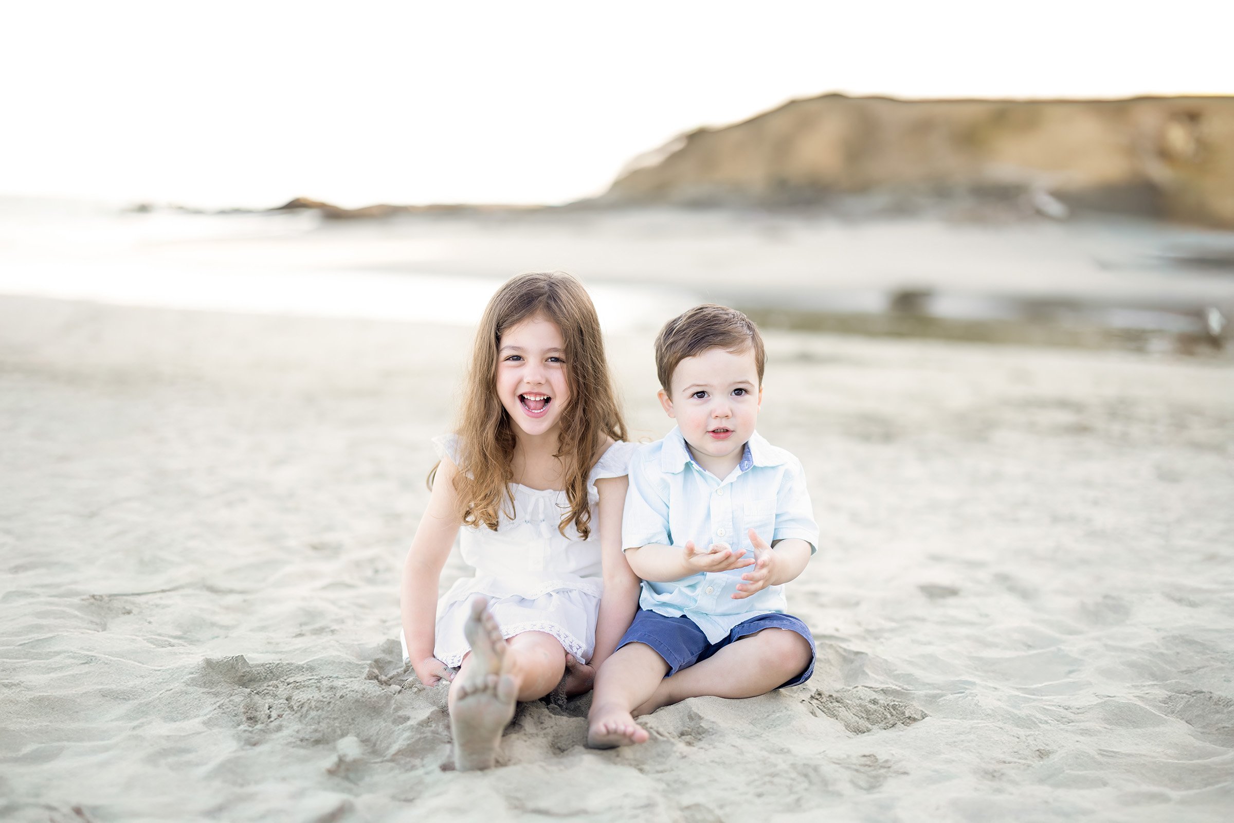 A brother and sister sitting in the sand at Avila Beach, enjoying a relaxed, candid moment by the ocean.