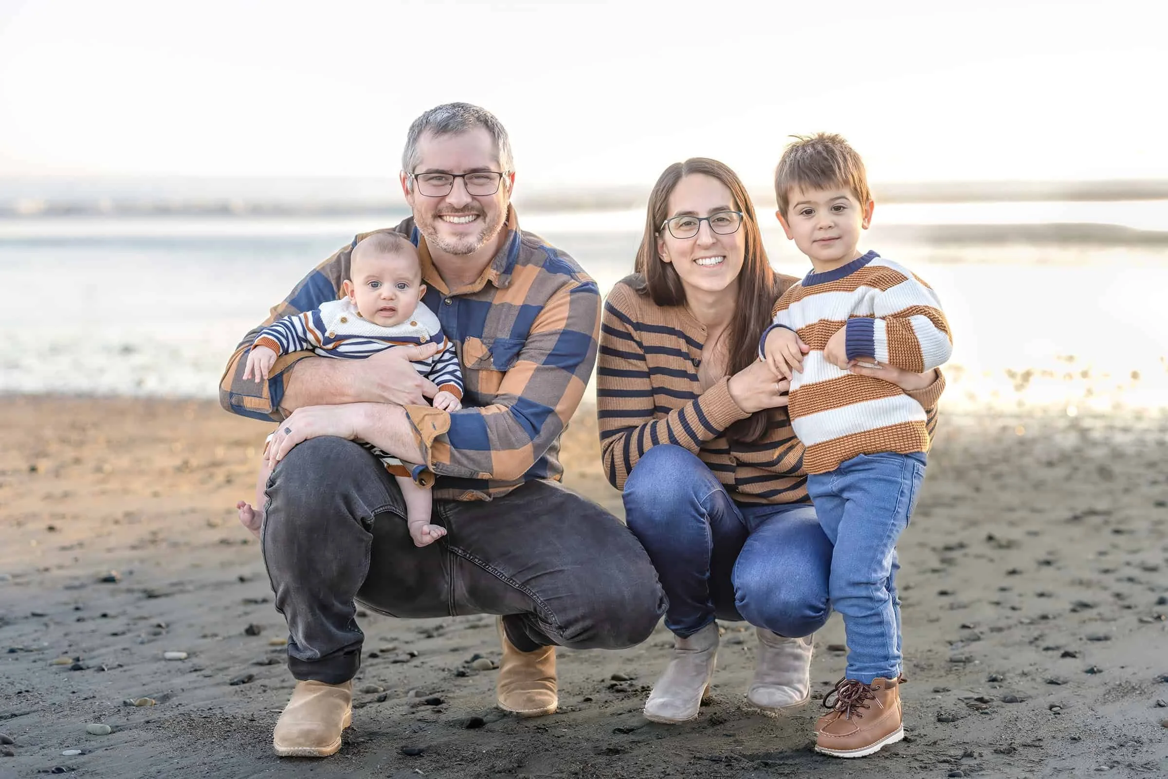 Family kneeling together by the water with their two children during a sunset photo session at Avila Beach on the Central Coast
