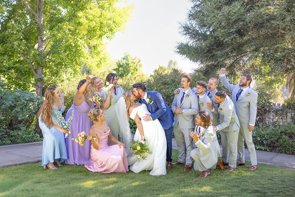 Groom kissing the bride as their bridal party cheers around them at Heritage House in Arroyo Grande, California