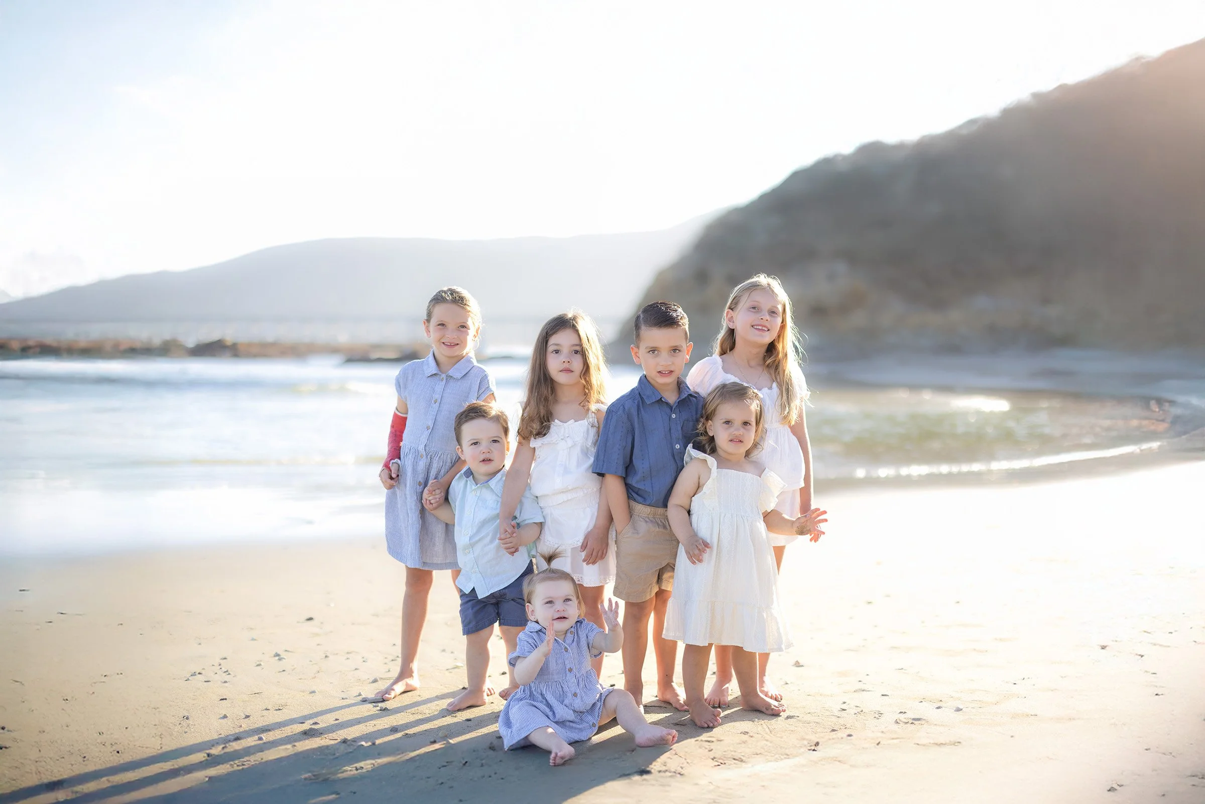 A group of siblings standing together at the shoreline in Avila Beach, captured during golden hour with soft fall tones and gentle ocean waves.