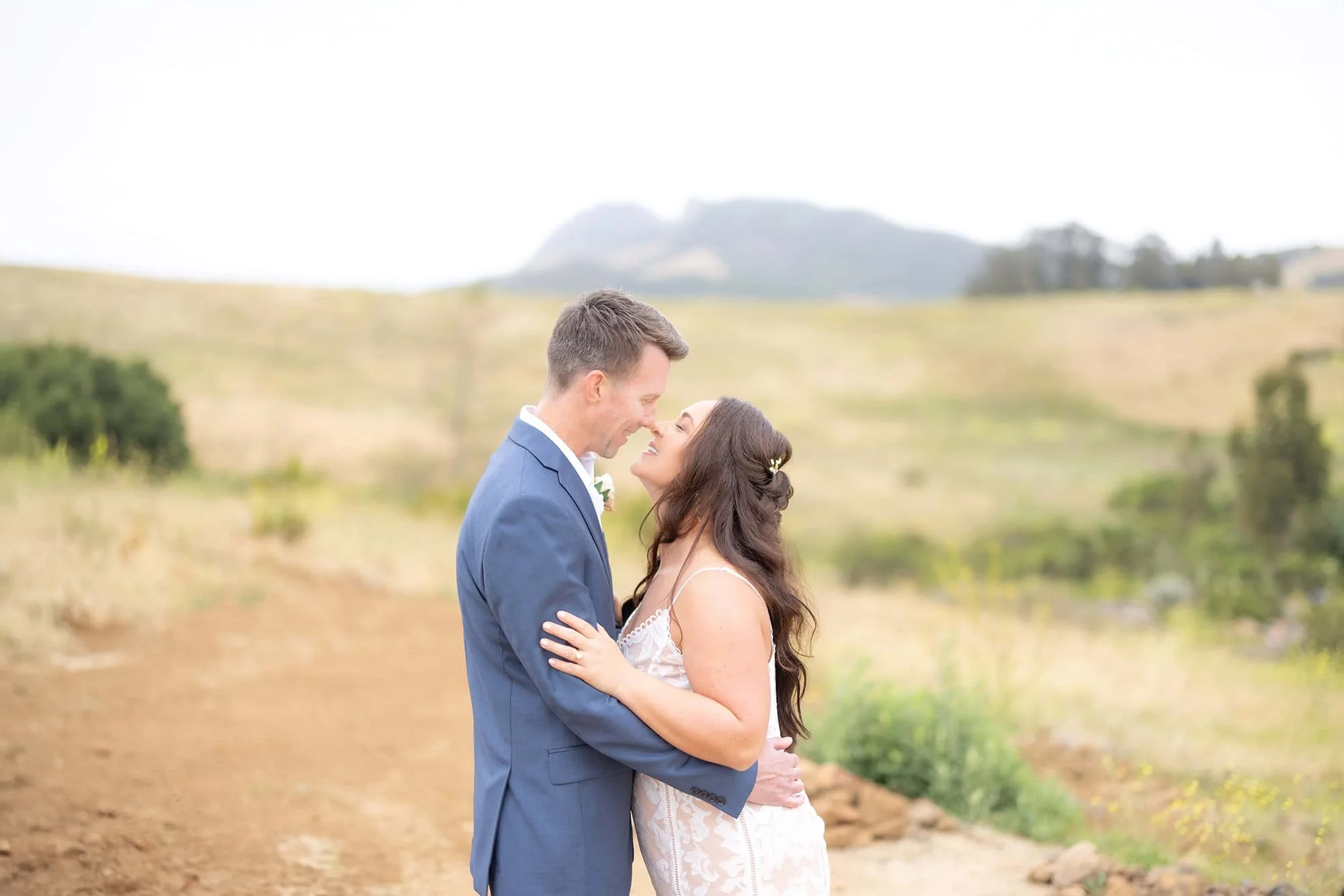 Bride and groom touching noses on a gravel trail surrounded by California wildflowers at the San Luis Obispo Botanical Garden