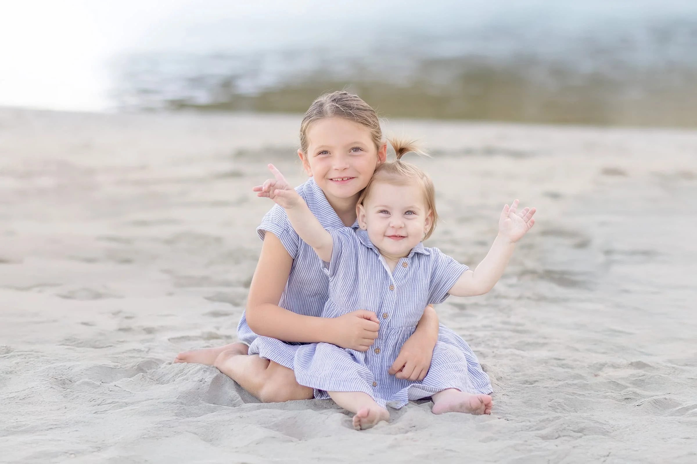 Two sisters sitting near the water’s edge at Avila Beach, sharing a quiet moment with the waves rolling in behind them.