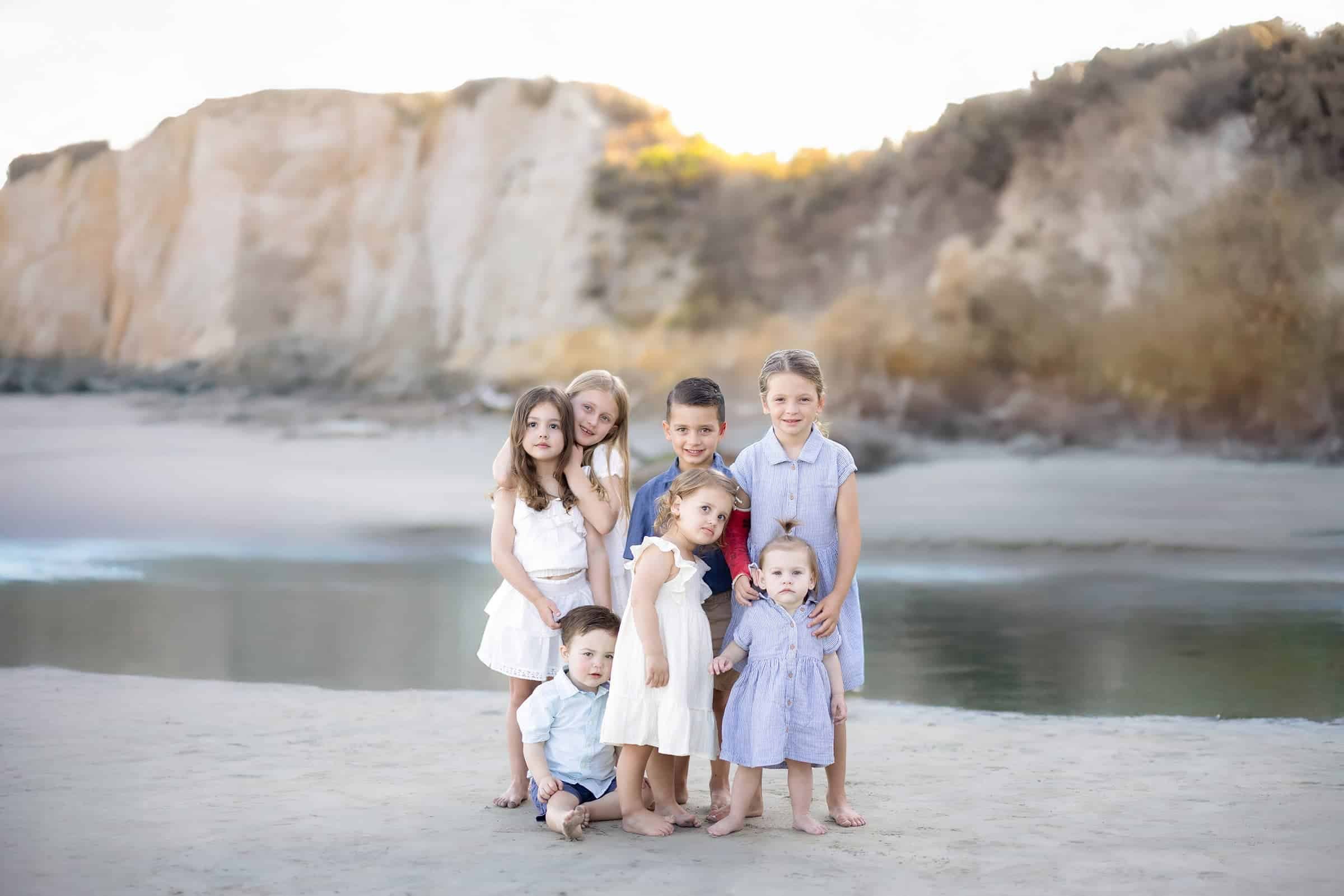 A group of siblings standing along the shoreline at Avila Beach, with the Central Coast cliffs rising behind them in warm evening light.