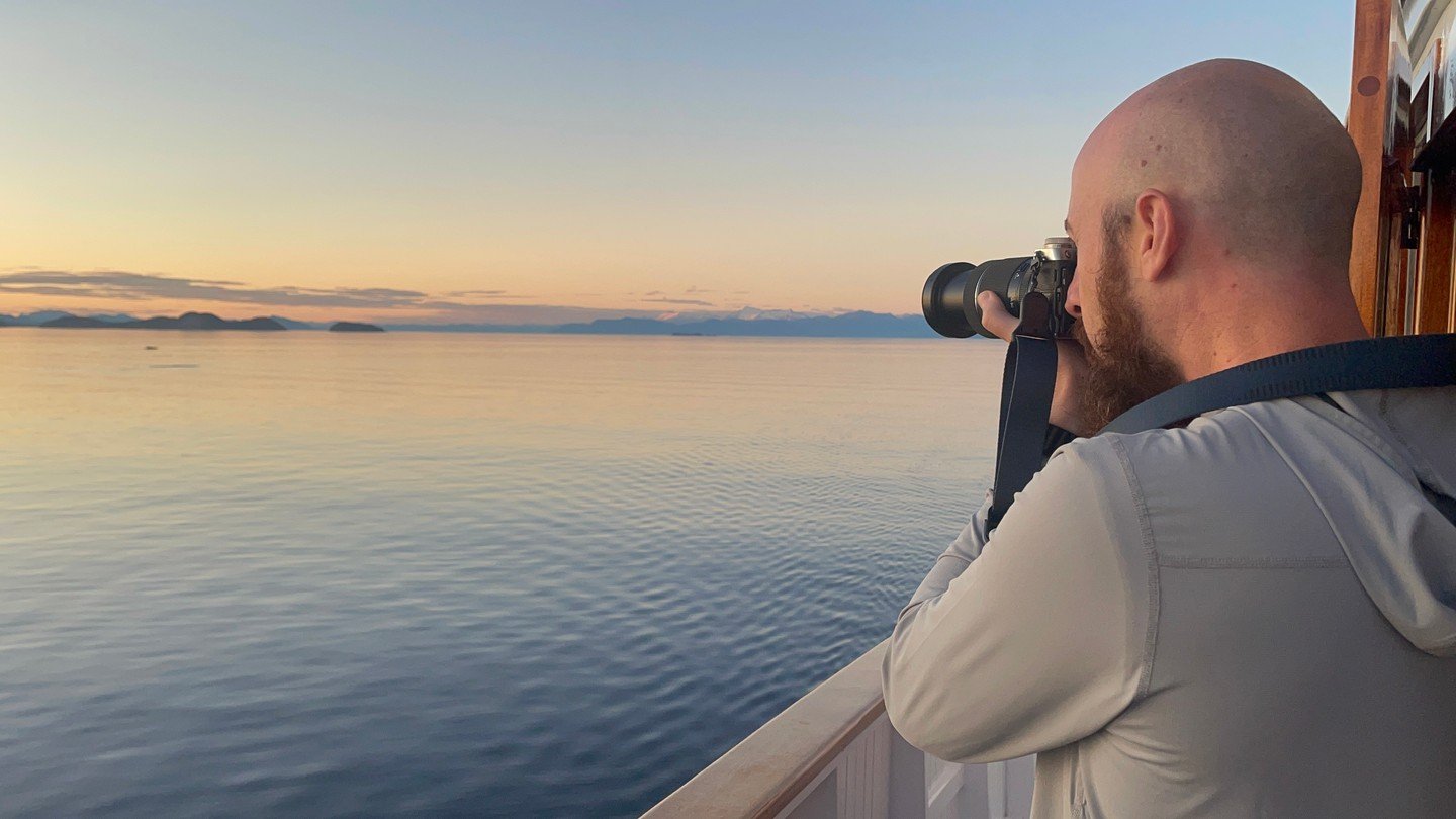 There&rsquo;s something about this light&mdash;blue and gold hues mixed&mdash;that makes even a quiet stretch of water feel infinite.

One of our guests paused here on the deck, camera in hand, catching the stillness that defines the Inside Passage. 
