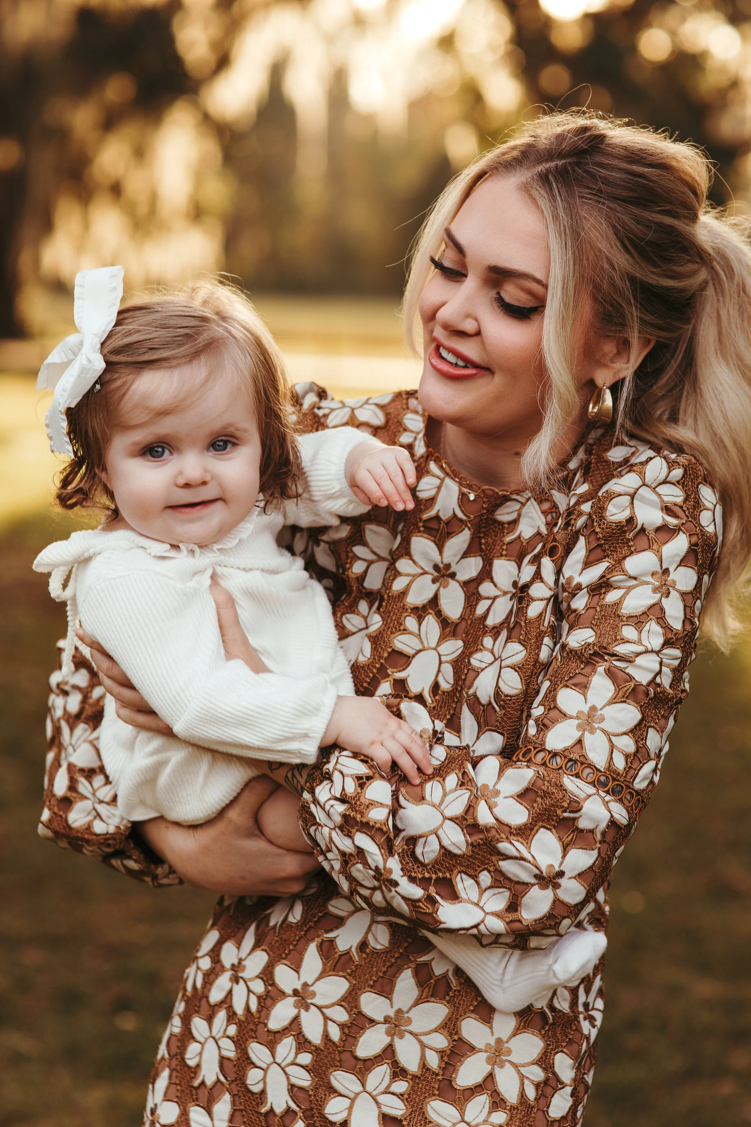 A woman holding a young girl outdoors during golden hour.