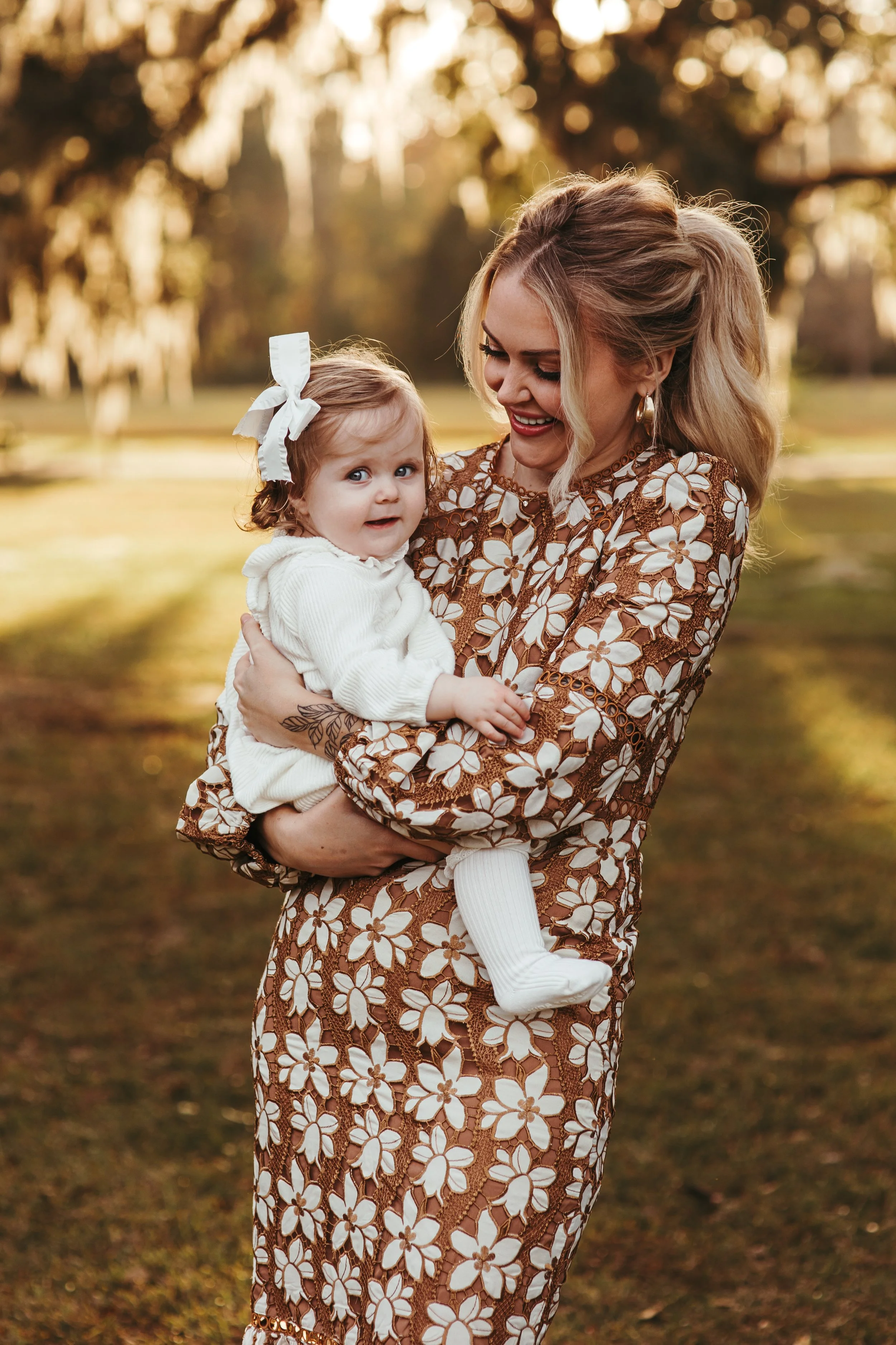 a woman with blonde hair holding a young girl in a park during sunset, both smiling