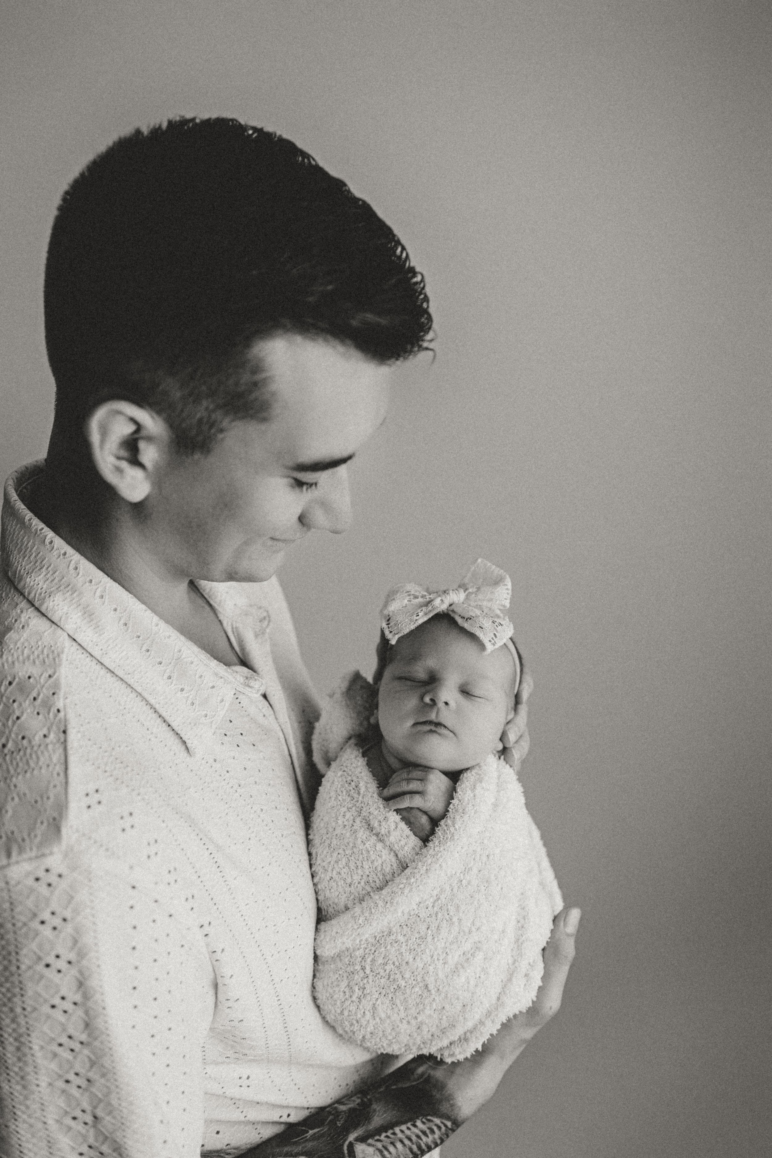 A man holding a newborn baby wrapped in a towel, both with closed eyes, in a black and white photo.