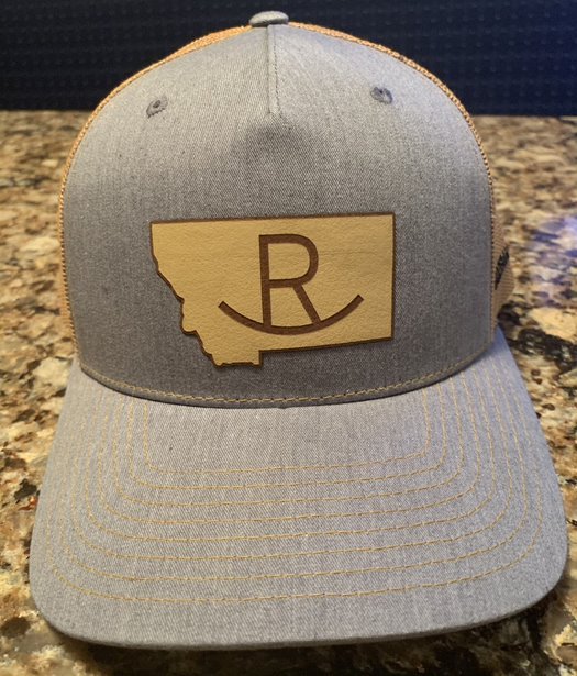 Light Gray Front and Gold Mesh Back, Trucker Cap with a gold patch on the front that is in the shape of Montana with the R Bar icon centered in the middle.