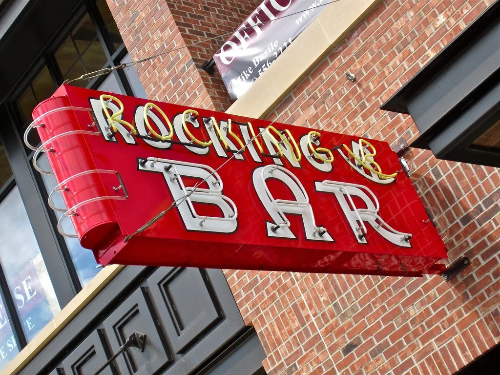 Red neon sign with text 'ROCKING R BAR' mounted on a brick building exterior.