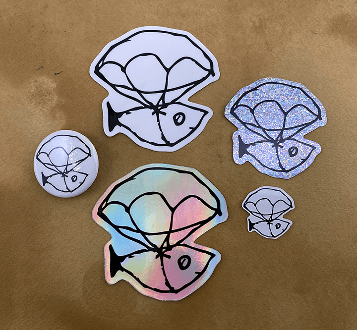 Five paper cutouts of a fish, resembling a stylized fish sketch, arranged on a brown surface. The cutouts vary in size and design, with some having holographic or glitter effects.