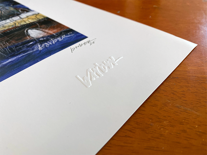 Close-up of a printed photograph on white matte paper with embossed text and a signature, resting on a wooden surface.