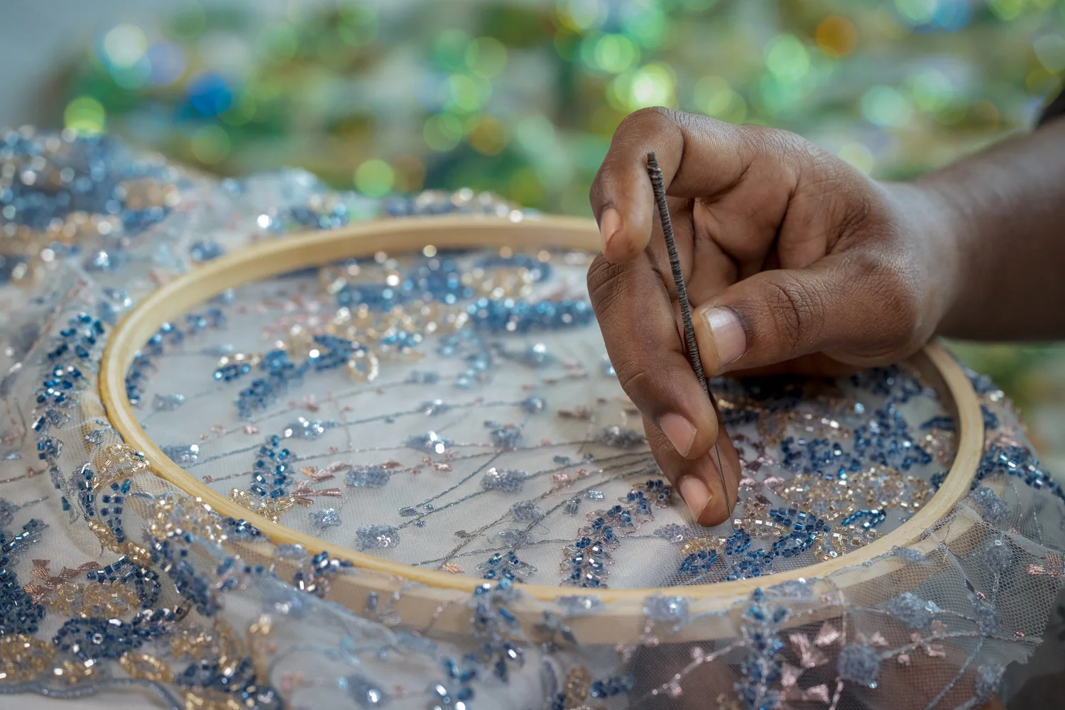 An artisan setting beads into blue floral embroidery by hand.