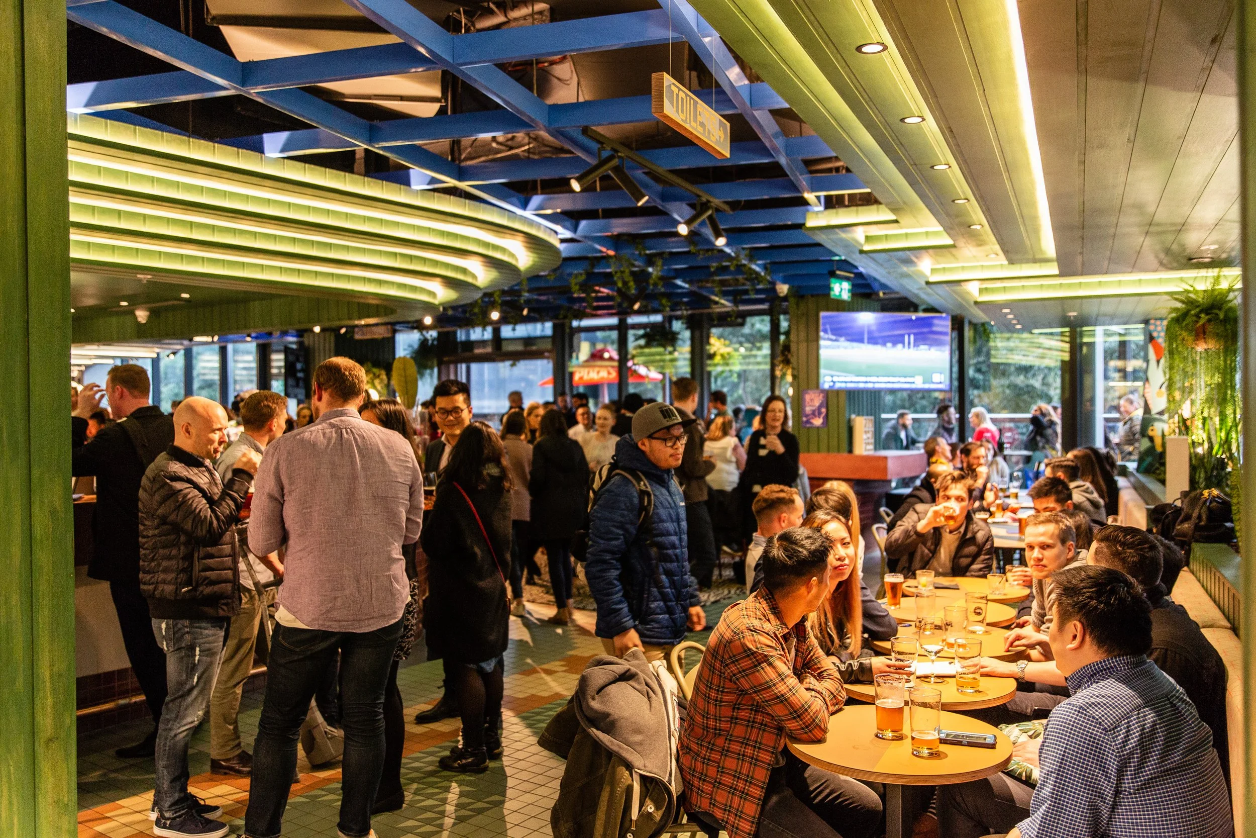 Hightail Bar in the Docklands with people socializing and enjoying drinks, with a green and yellow color theme and decorative plants.