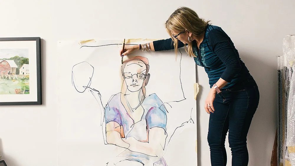 Clare Stokolosa artist focused on drawing on a piece of paper with a brush, showcasing her artistic skills.