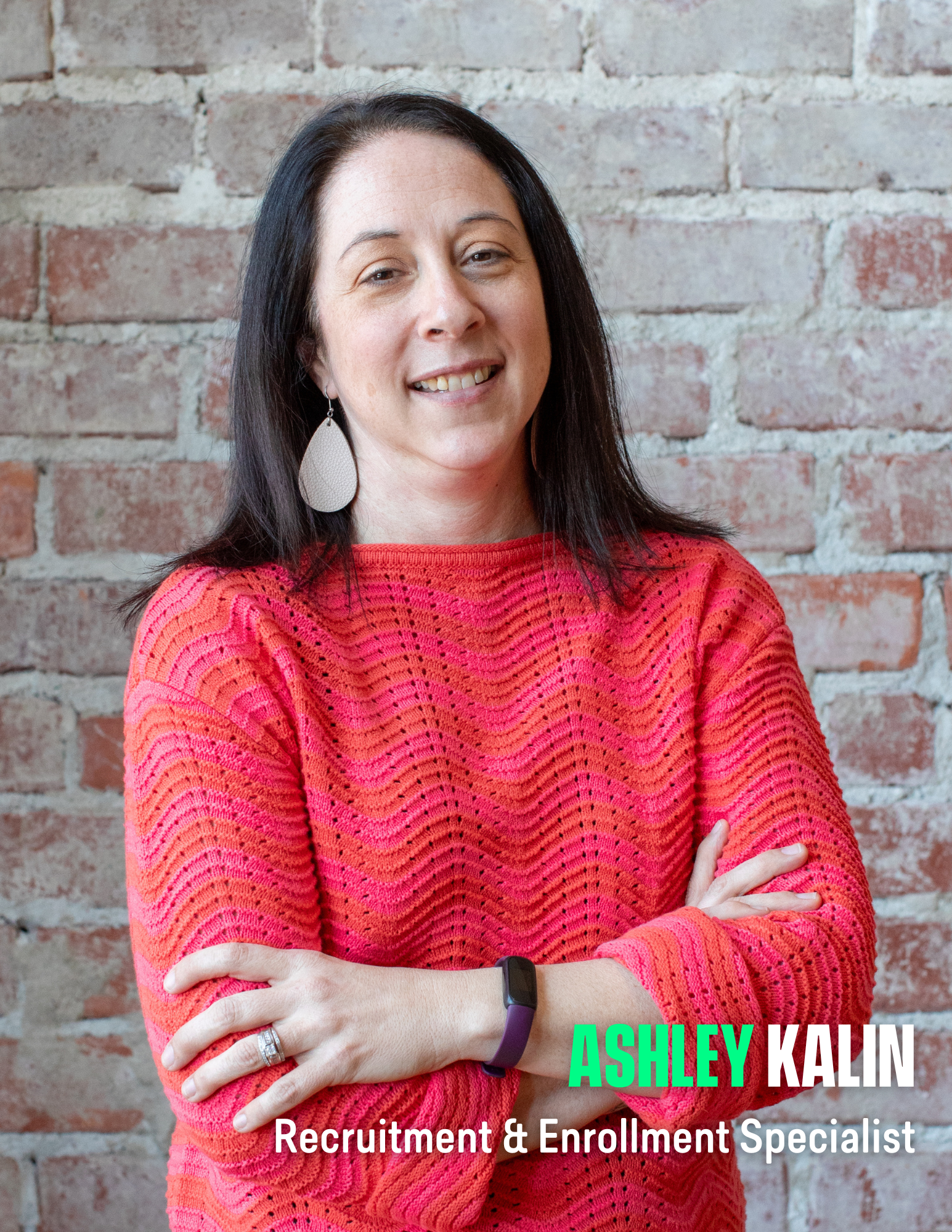 Photo of a woman with dark hair wearing an orange and pink sweater in front of a brick wall.