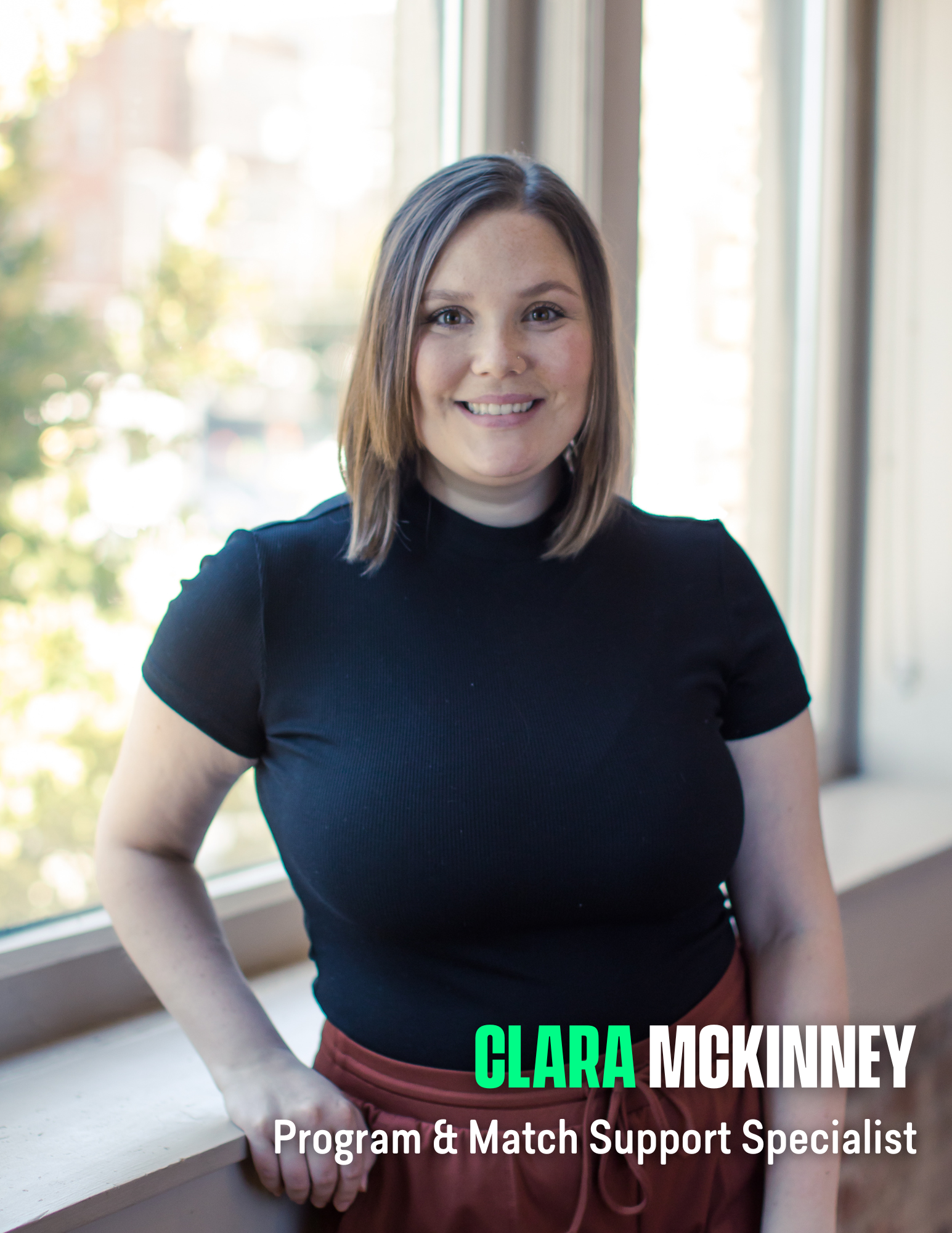 Photo of a woman with a short bob haircut, blonde, with a black shirt in front of a window.