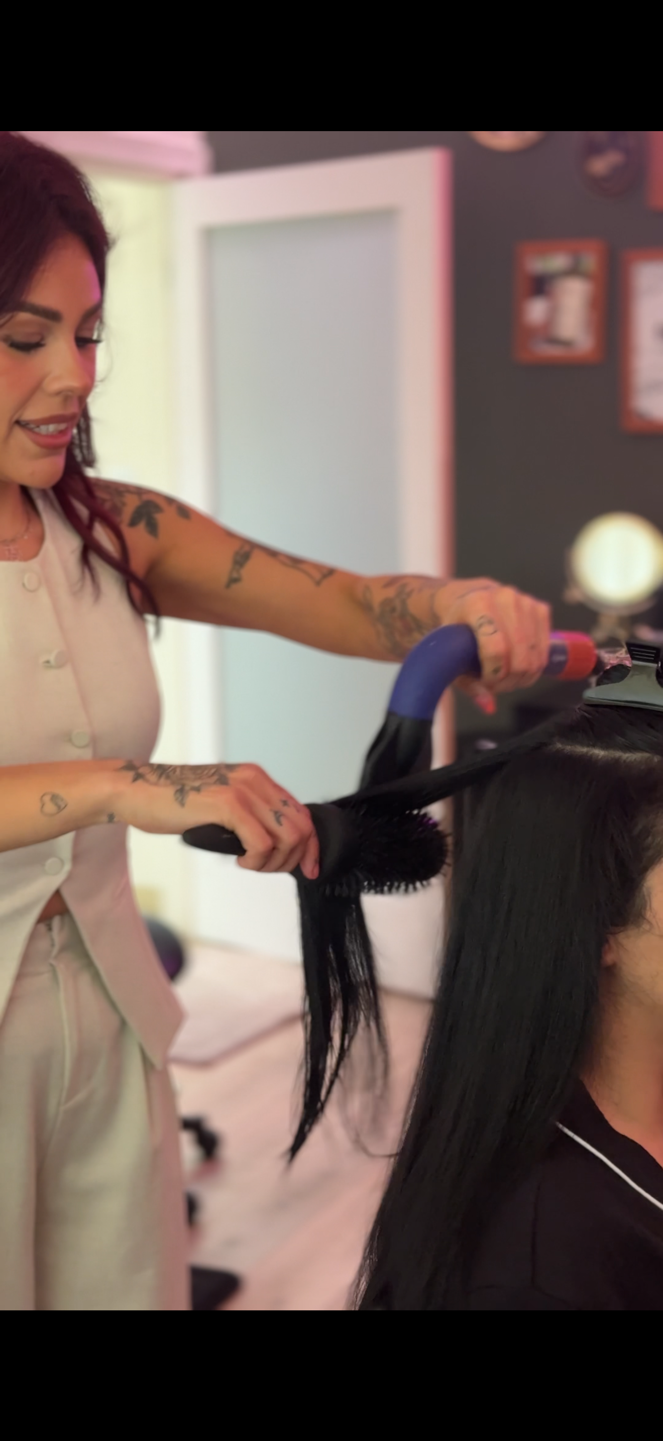 Woman with tattoos blow-drying another person's long black hair in a salon. blowout style, wash and style, haircare, hair washing and styling services, fresno hairstylist, 559 blowout bar