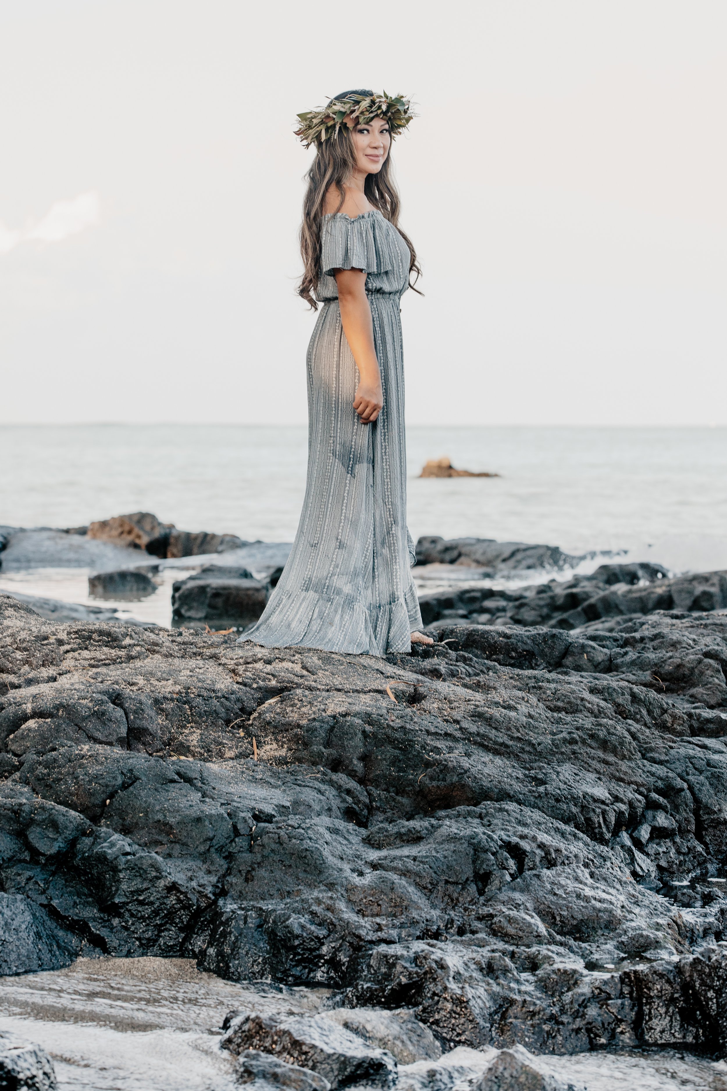 Dr. Maria Grace Wolk standing on ocean rocks wearing a floral lei