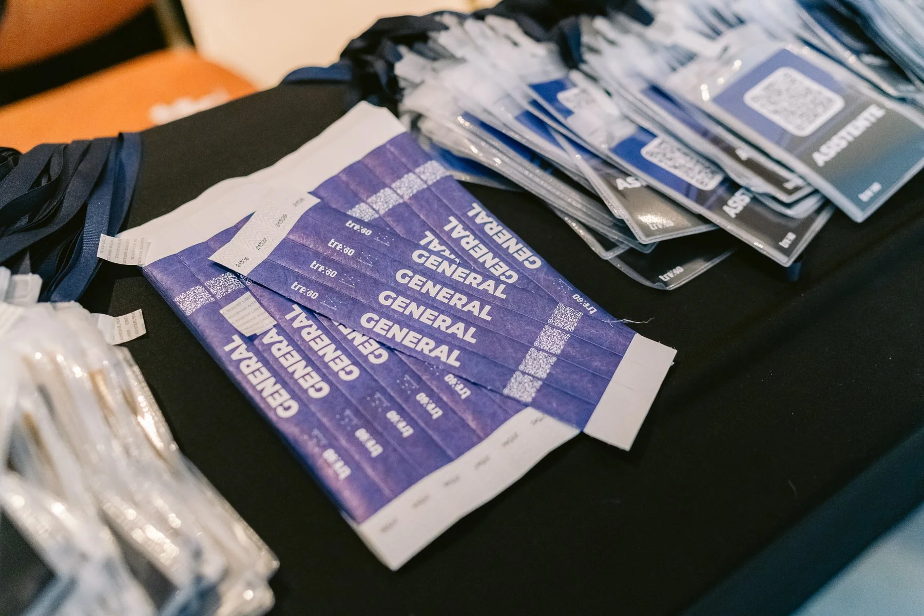 Entradas impresas que dicen 'GENERAL' y un código QR, sobre una mesa con fondo oscuro, probablemente en un evento o conferencia en un recinto cerrado.